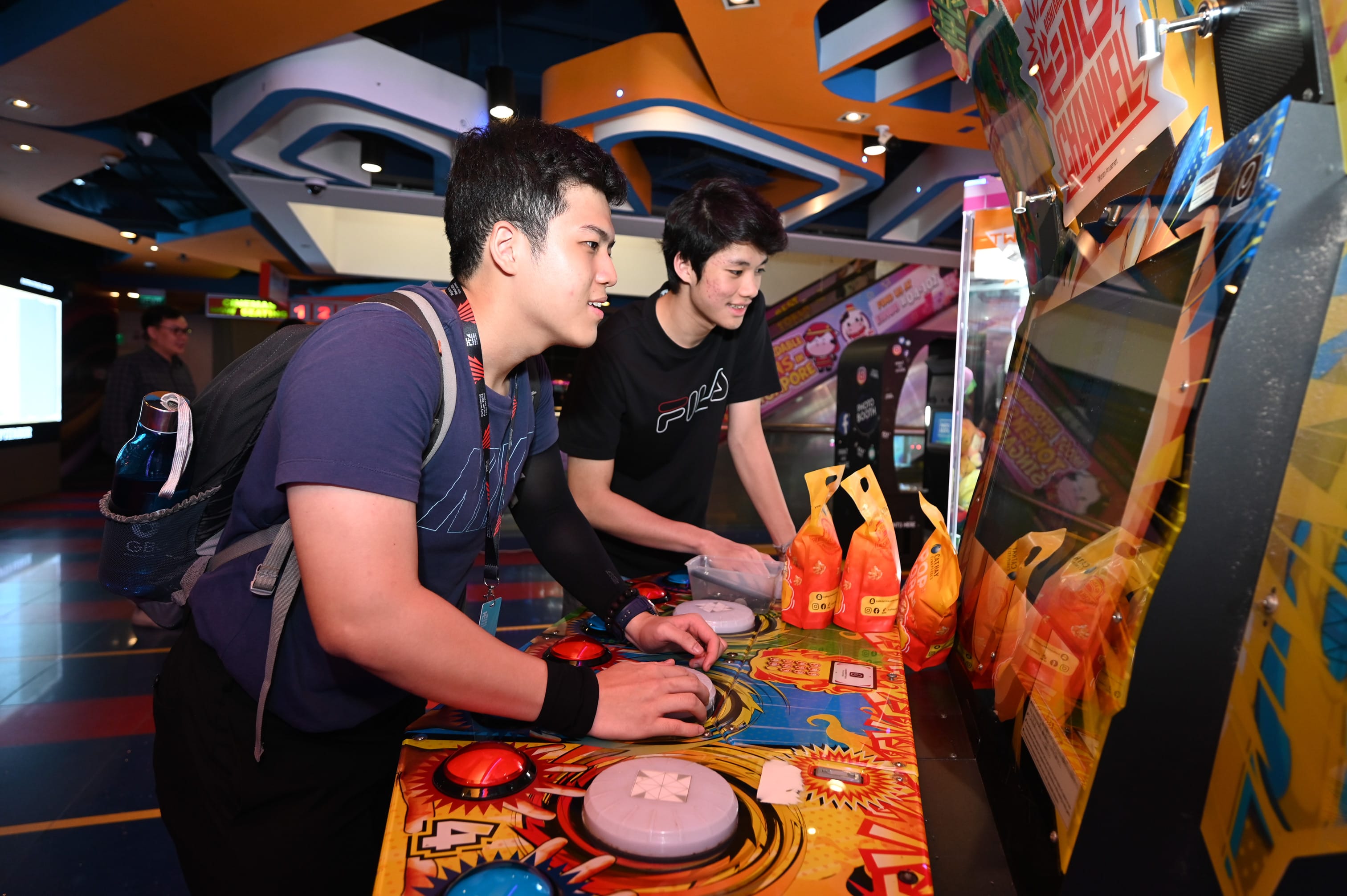Two young men playing a colorful arcade machine in a bright indoor arcade center.