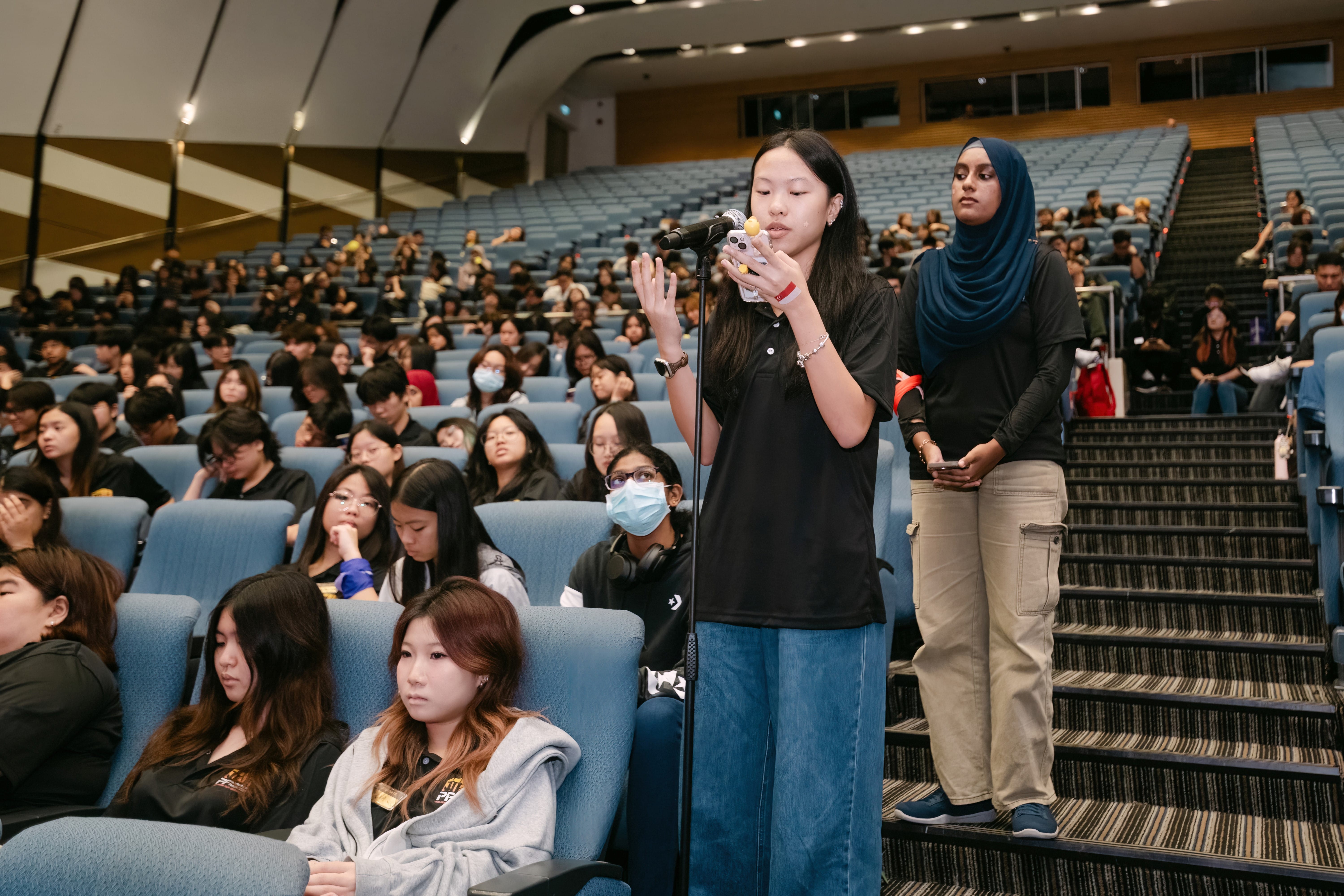 A young woman speaks into a microphone while holding her handphone.