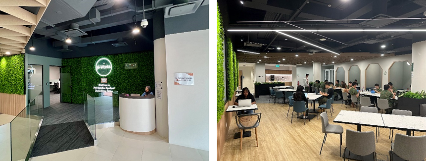 Modern co-working space showing a reception desk with green walls on the left and a seating area with people working on laptops on the right.