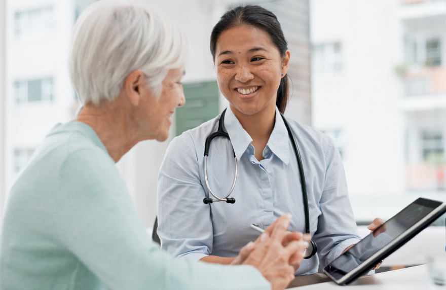 Doctor consulting elderly woman and reviewing health information on tablet.