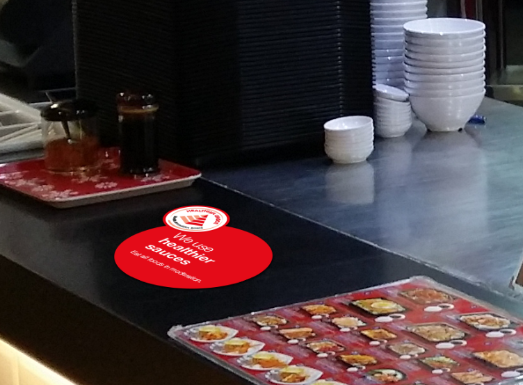 Food stall counter displaying sign that healthier sauces are used for meals.