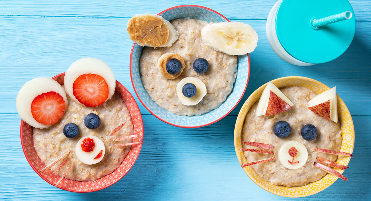 Three bowls of oatmeal decorated with frruits to look like animal faces.