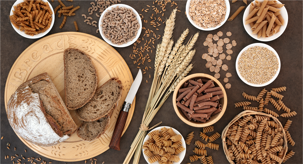 Assortment of wholegrain foods including bread, pasta, oats and wheat grains.