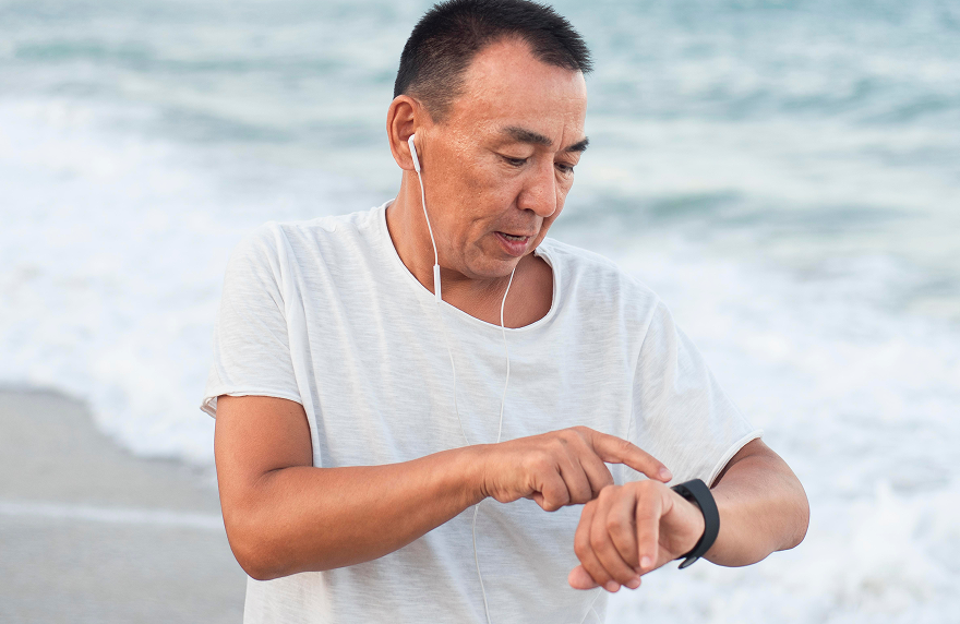 Man checking fitness tracker on smartwatch while exercising by the sea.