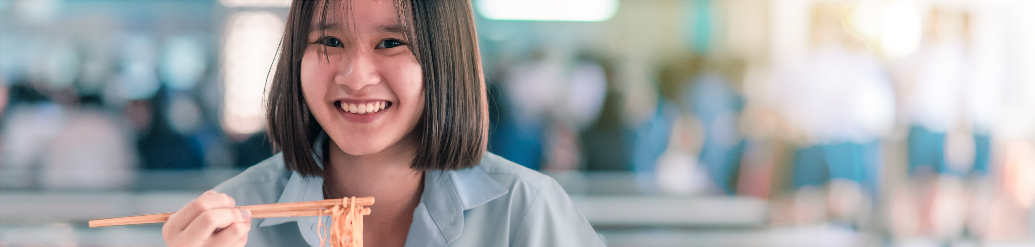 Young woman smiling while eating noodles with chopsticks in a dining setting.