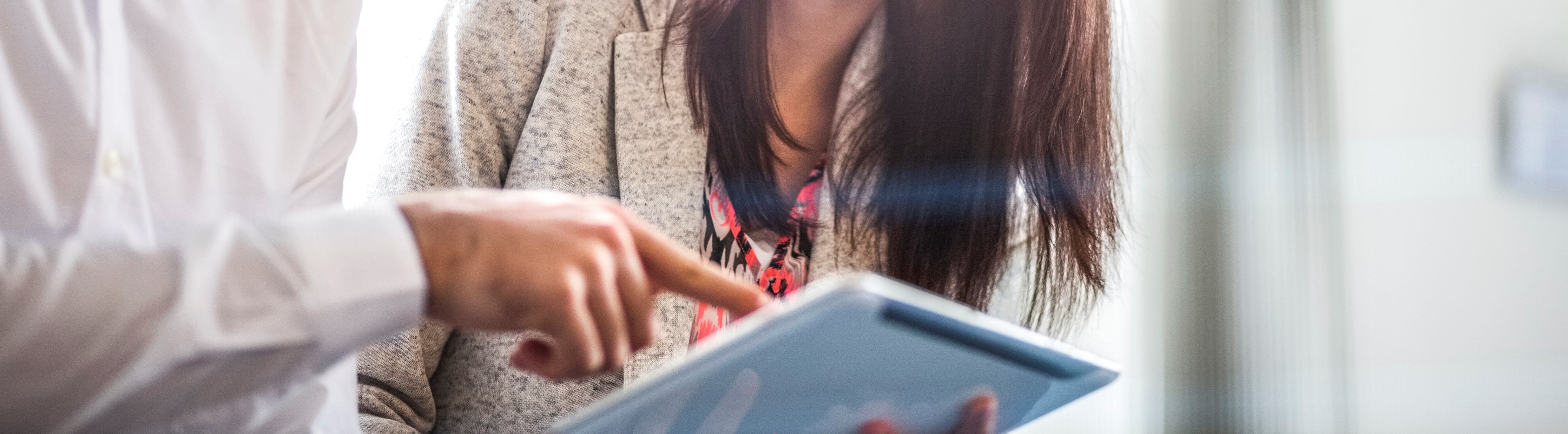 Two colleagues reviewing information together on a tablet in an office setting.