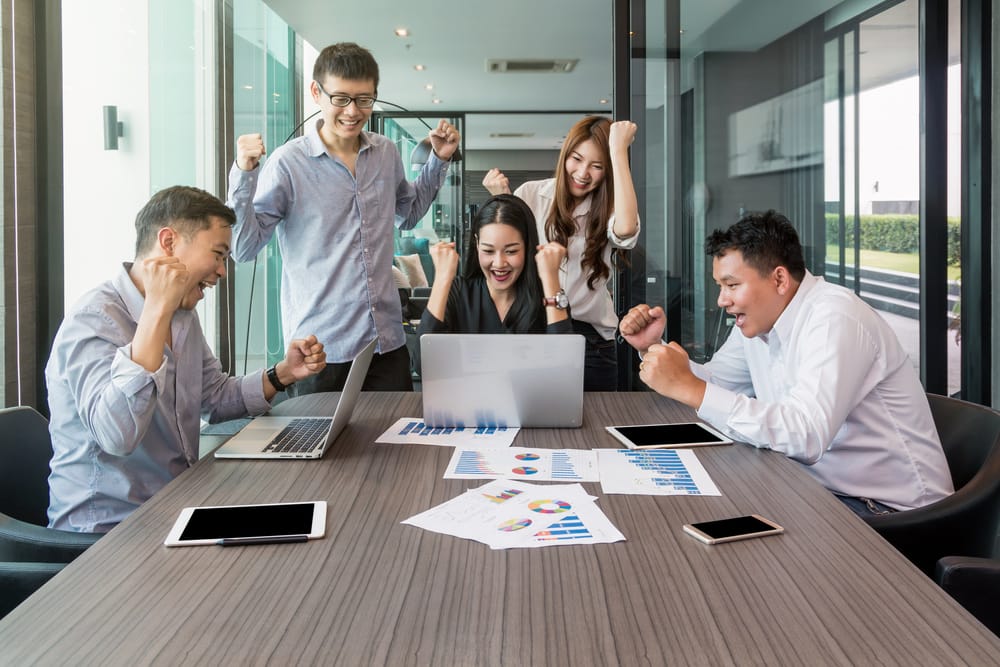 A group of colleagues cheering, with their arms gesturing, around a table.