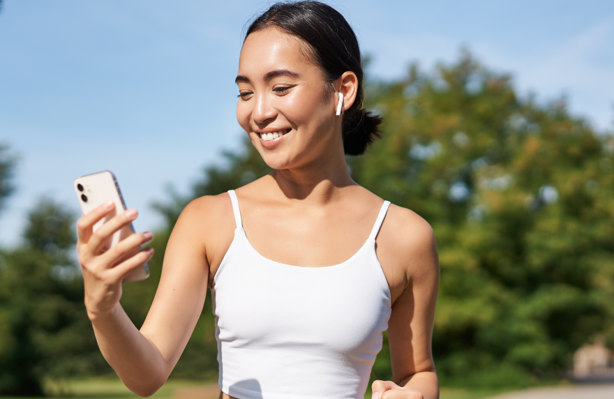Woman exercising outdoors while checking health app on smartphone.