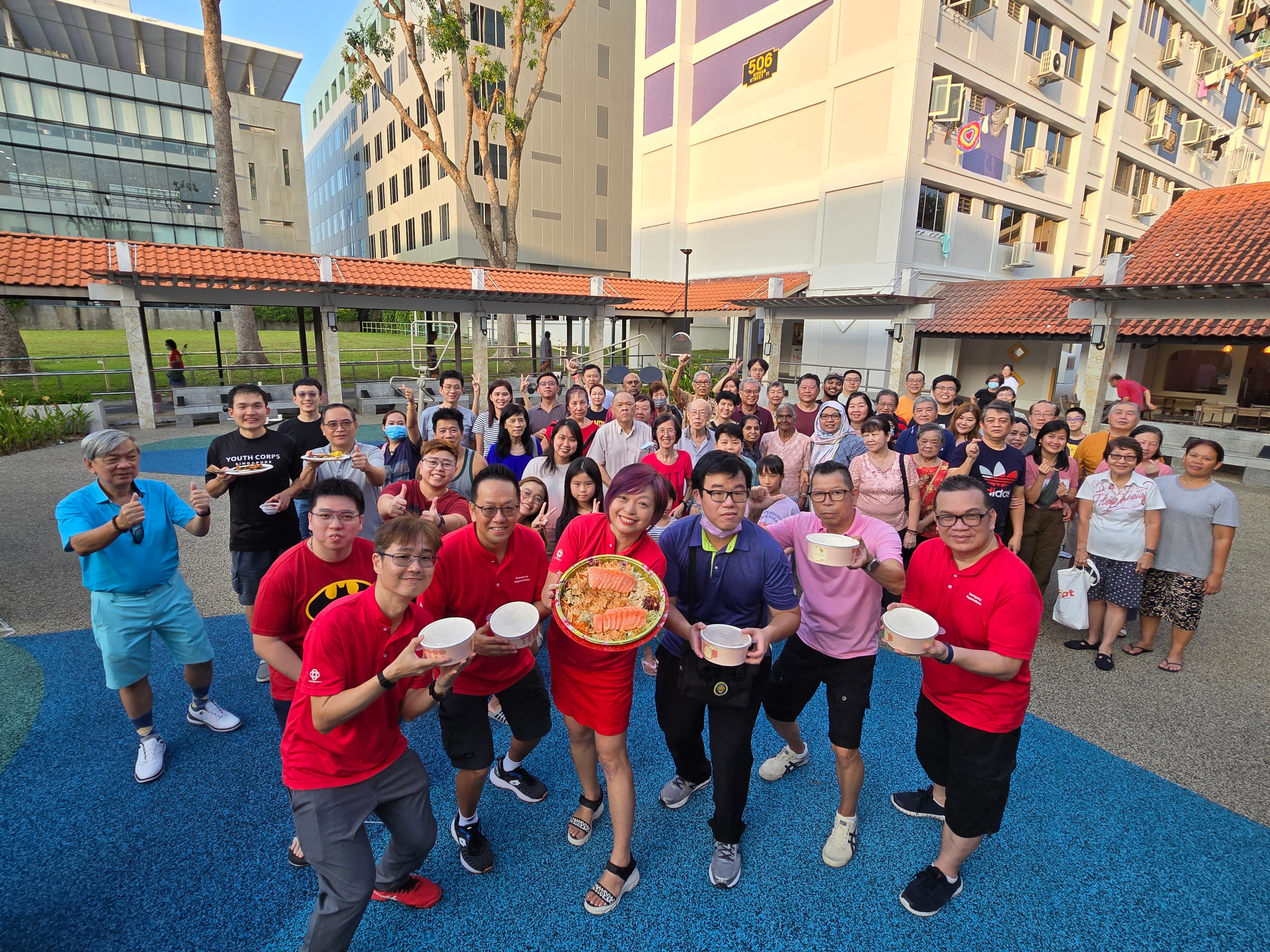Large group poses with food containers, building backdrop with street number 506.