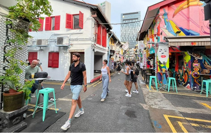 Street scene with people walking past colorful buildings and outdoor cafes.