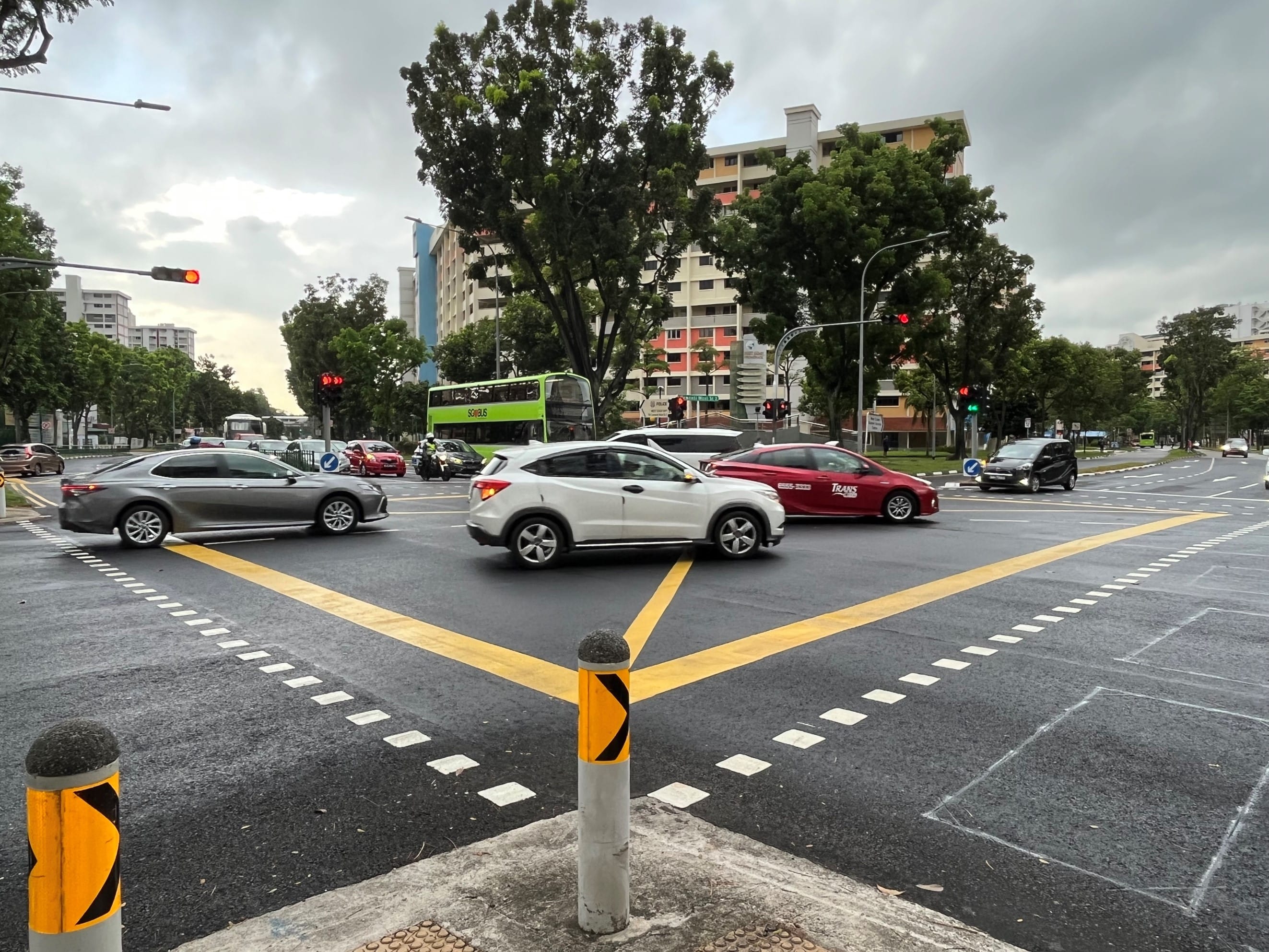 City intersection with cars, a green SBS Transit bus, yellow markings, and apartment buildings.