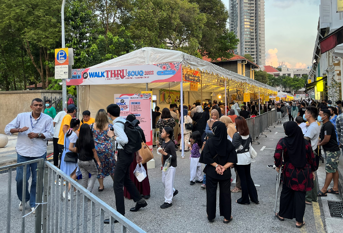 Crowd walking through "WalkThru Souq 2022" market tent, with barrier, street, and buildings.