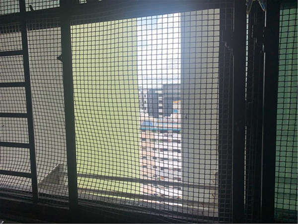 View through metal bars and safety netting towards a tall building.