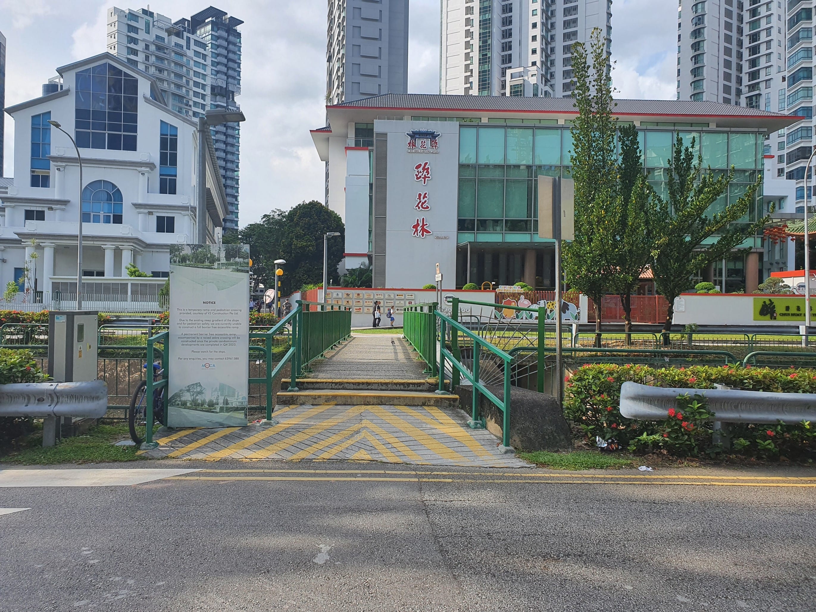 Street view of Chu Huay Lim Club with a pedestrian bridge and tall buildings.