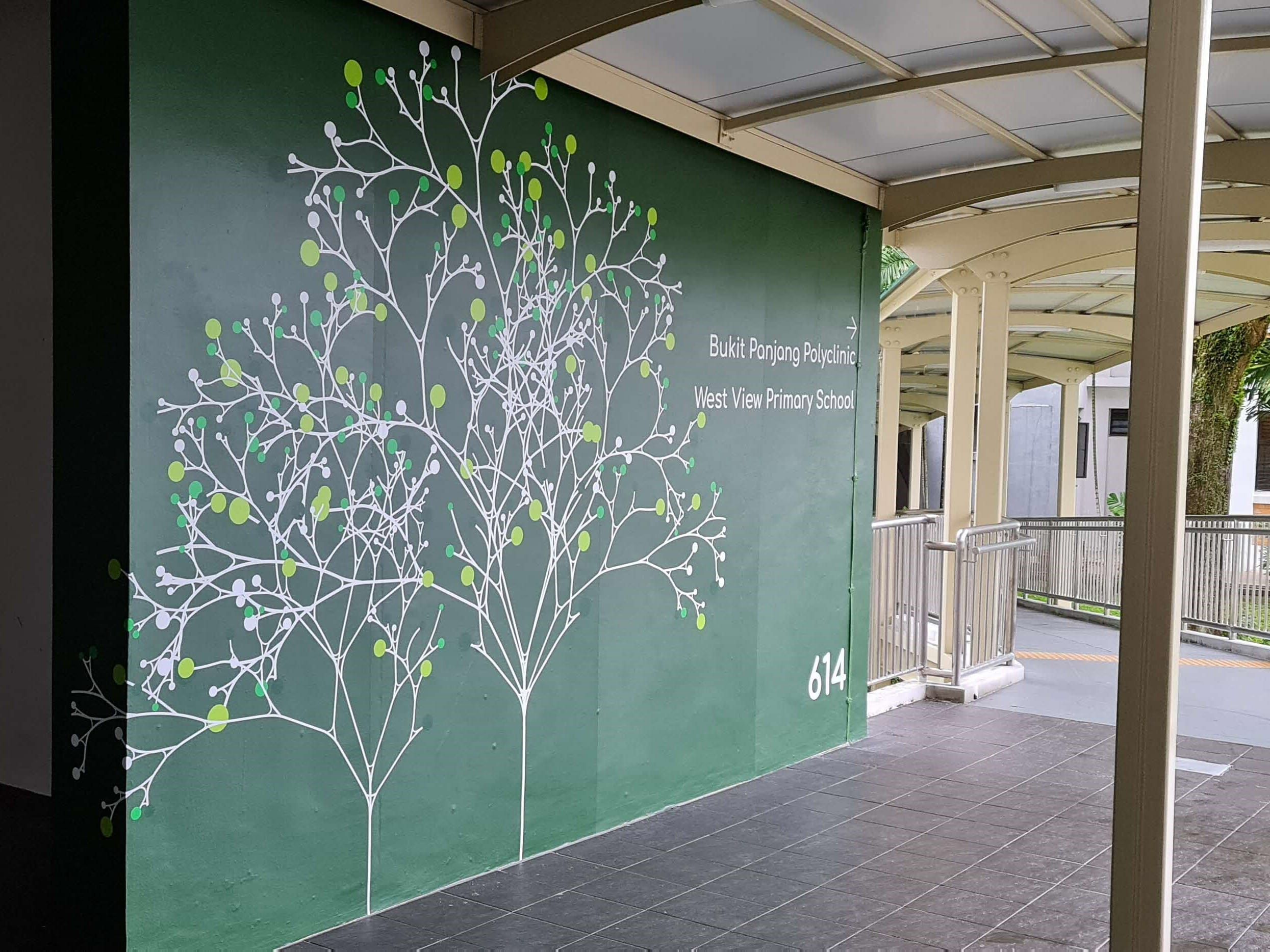 Olive wall with white tree branch art and text: Bukit Panjang Polyclinic, West View Primary School, number 614, path to building.