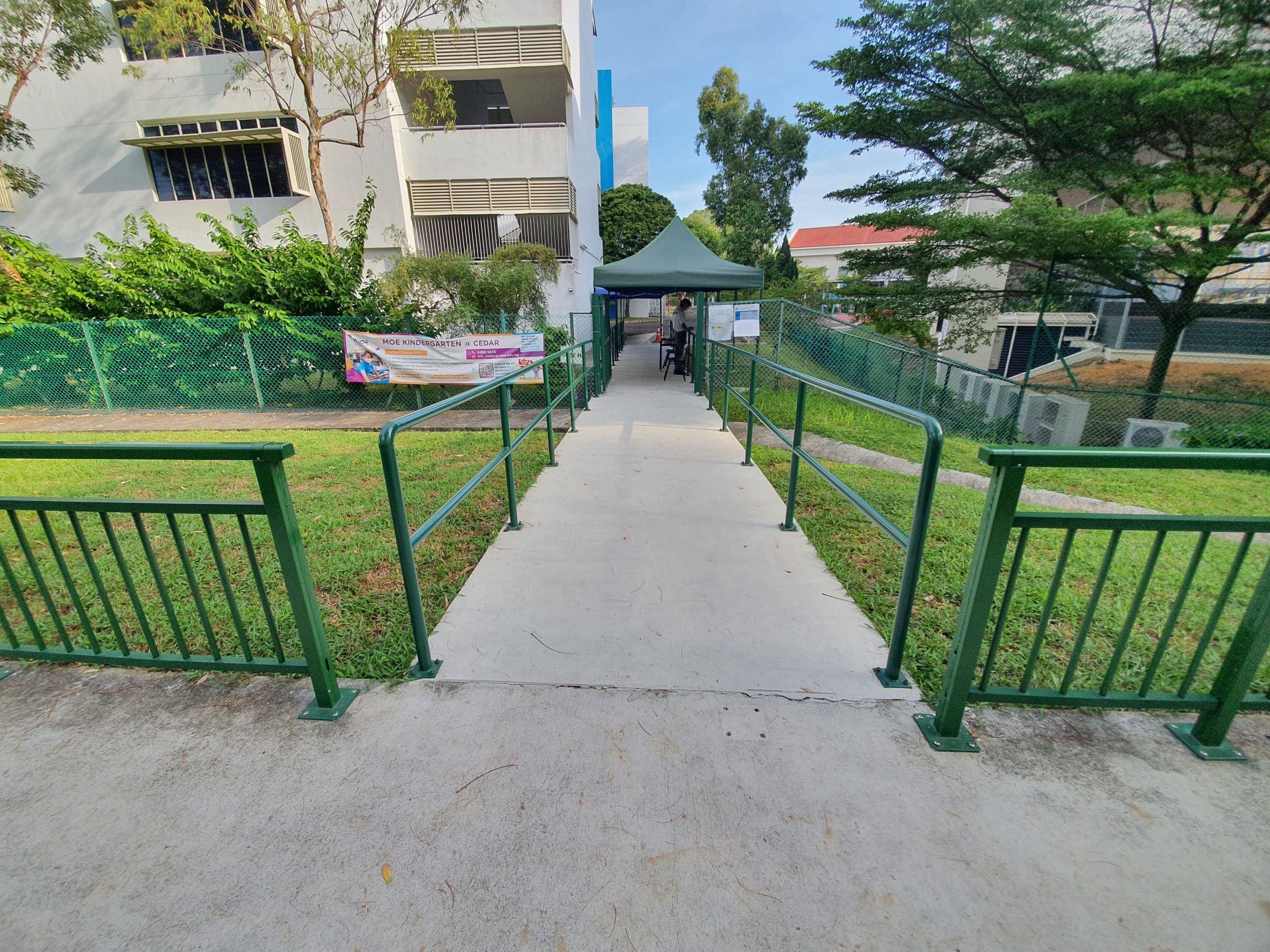 Concrete ramp with green handrails leads to a tent. "MOE Kindergarten" sign is visible.
