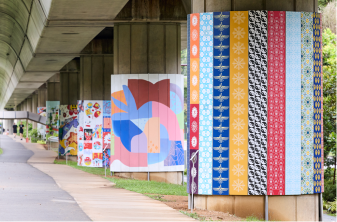 Murals on concrete supports under an overpass, along a pathway.