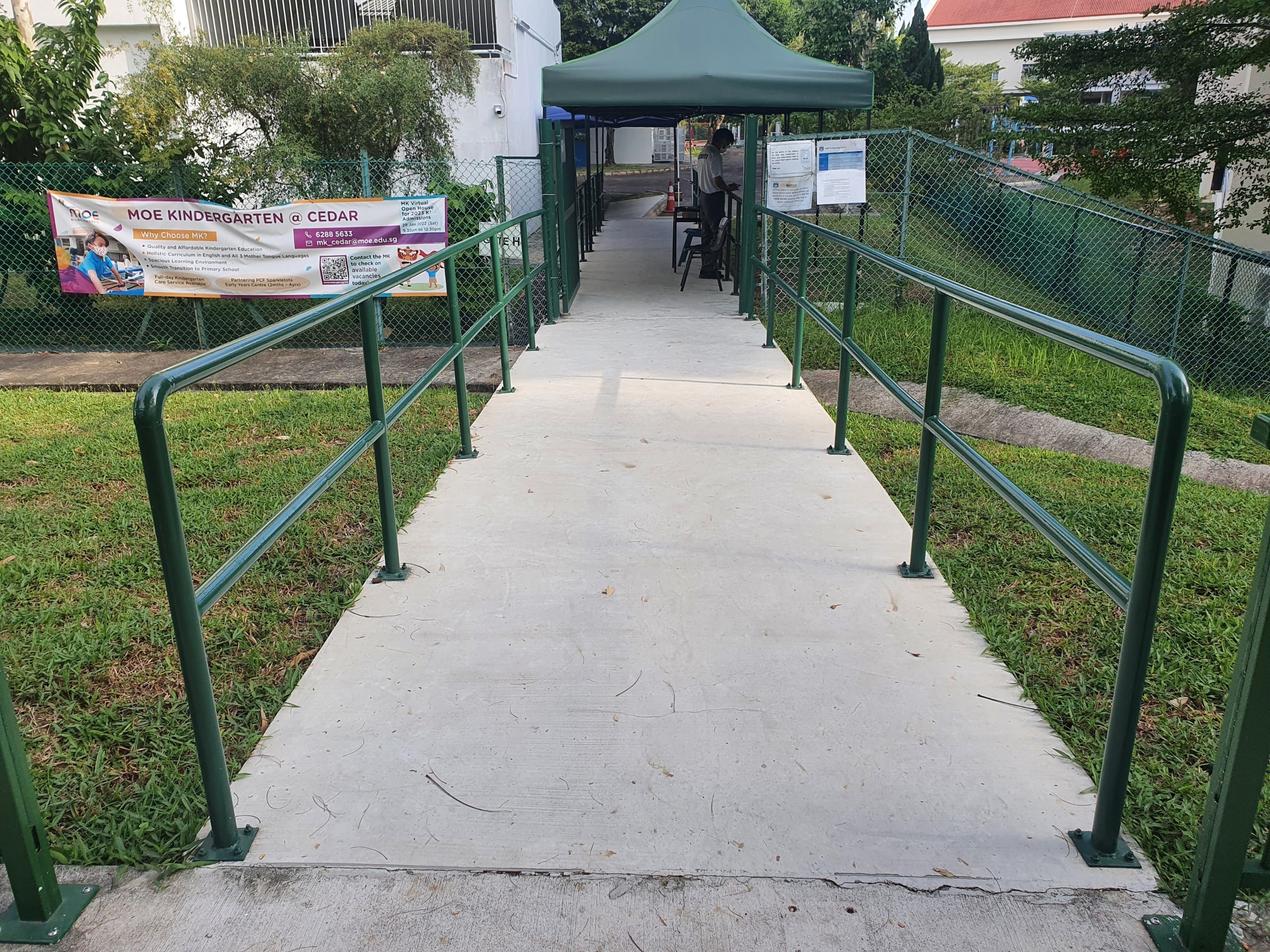 Concrete ramp with green railings leads to tent; MOE Kindergarten @ Cedar banner visible.