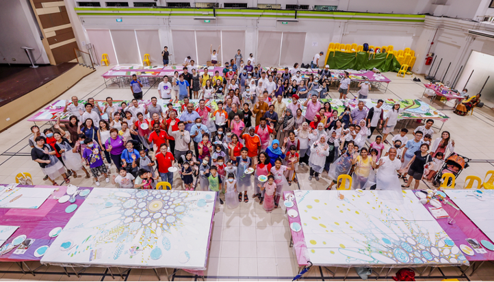Large group of people waving behind two painted canvases in a brightly lit hall.