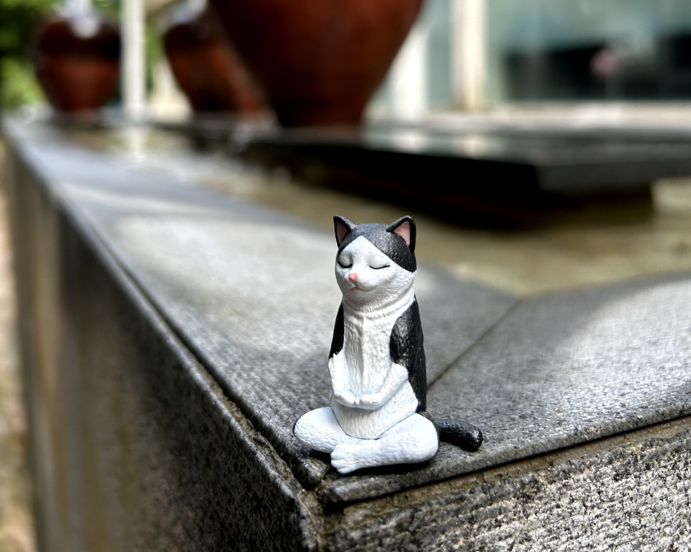 Small black and white cat figurine sitting in a cross-legged meditation pose on a gray stone ledge.