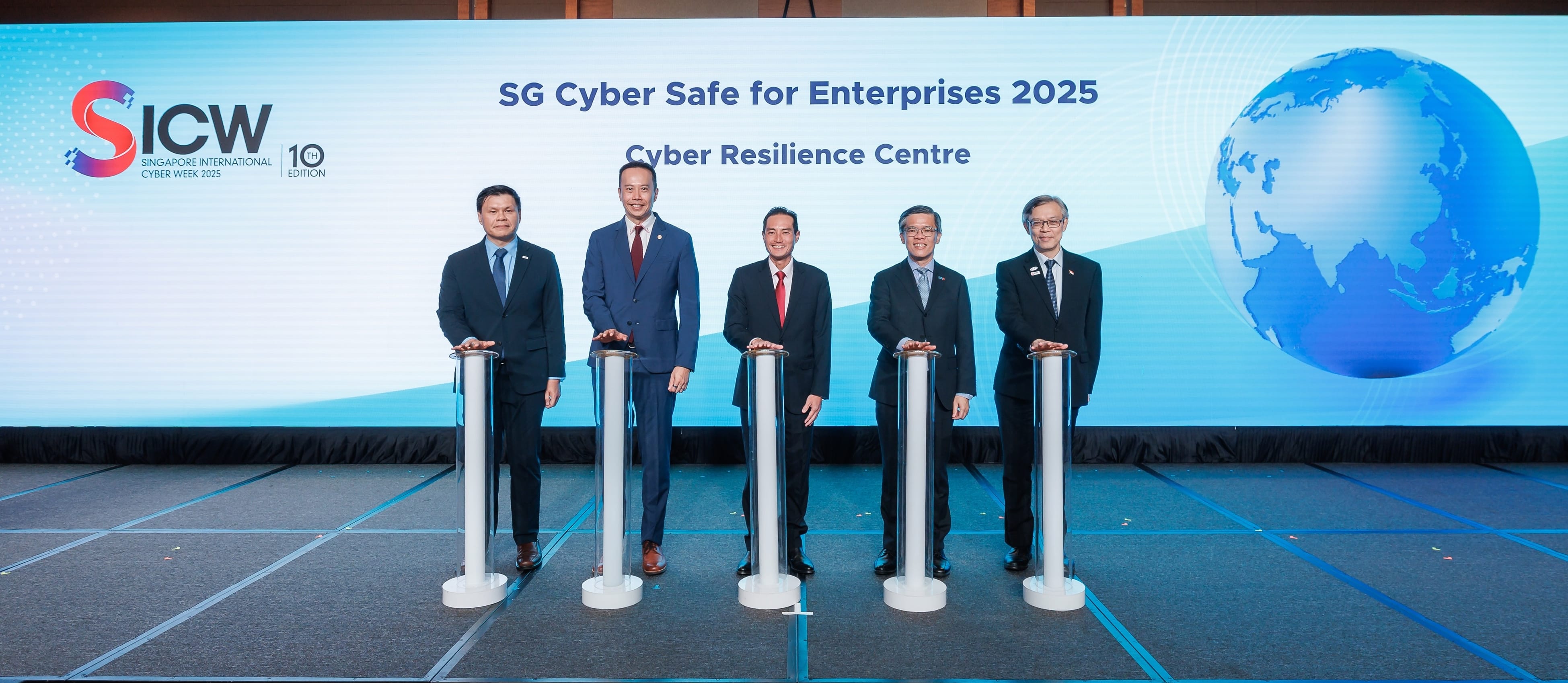 Five men in suits stand at podiums during the SICW 2025 launch of SG Cyber Safe for Enterprises Cyber Resilience Centre.