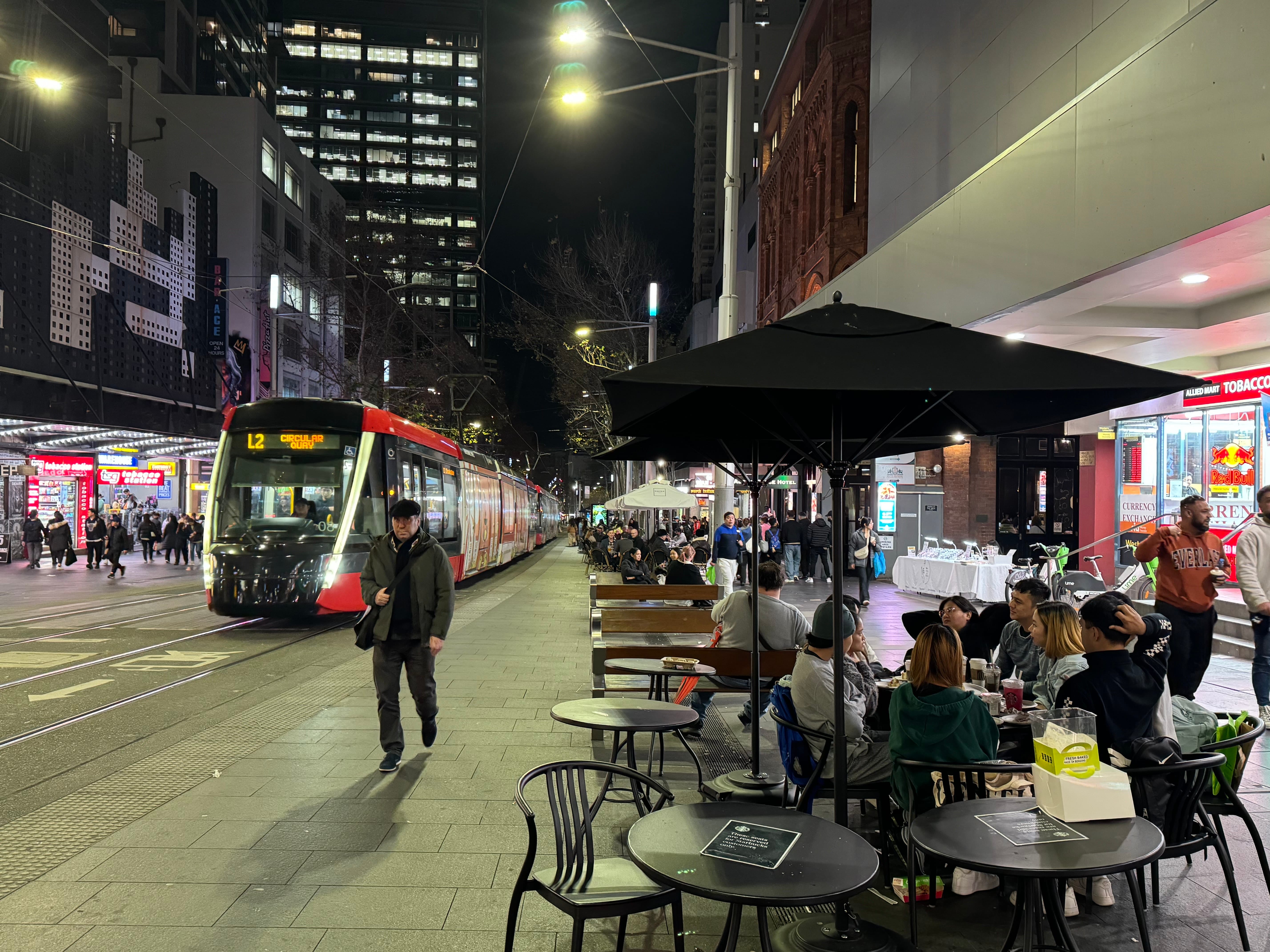 People sitting, eating and walking along George Street with and incoming subway