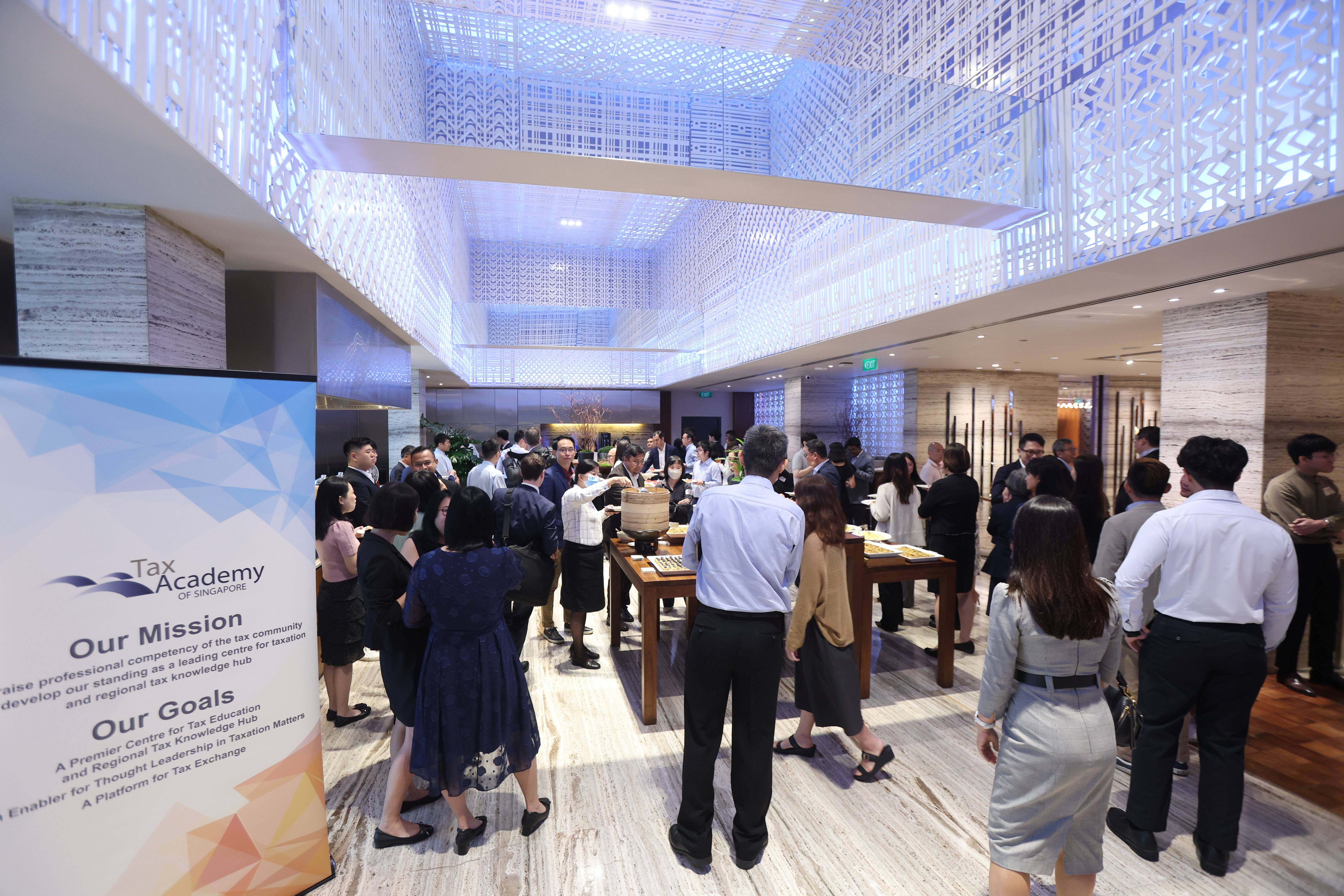 Professionals networking at a Tax Academy of Singapore event in an elegant venue with a decorative lit ceiling.