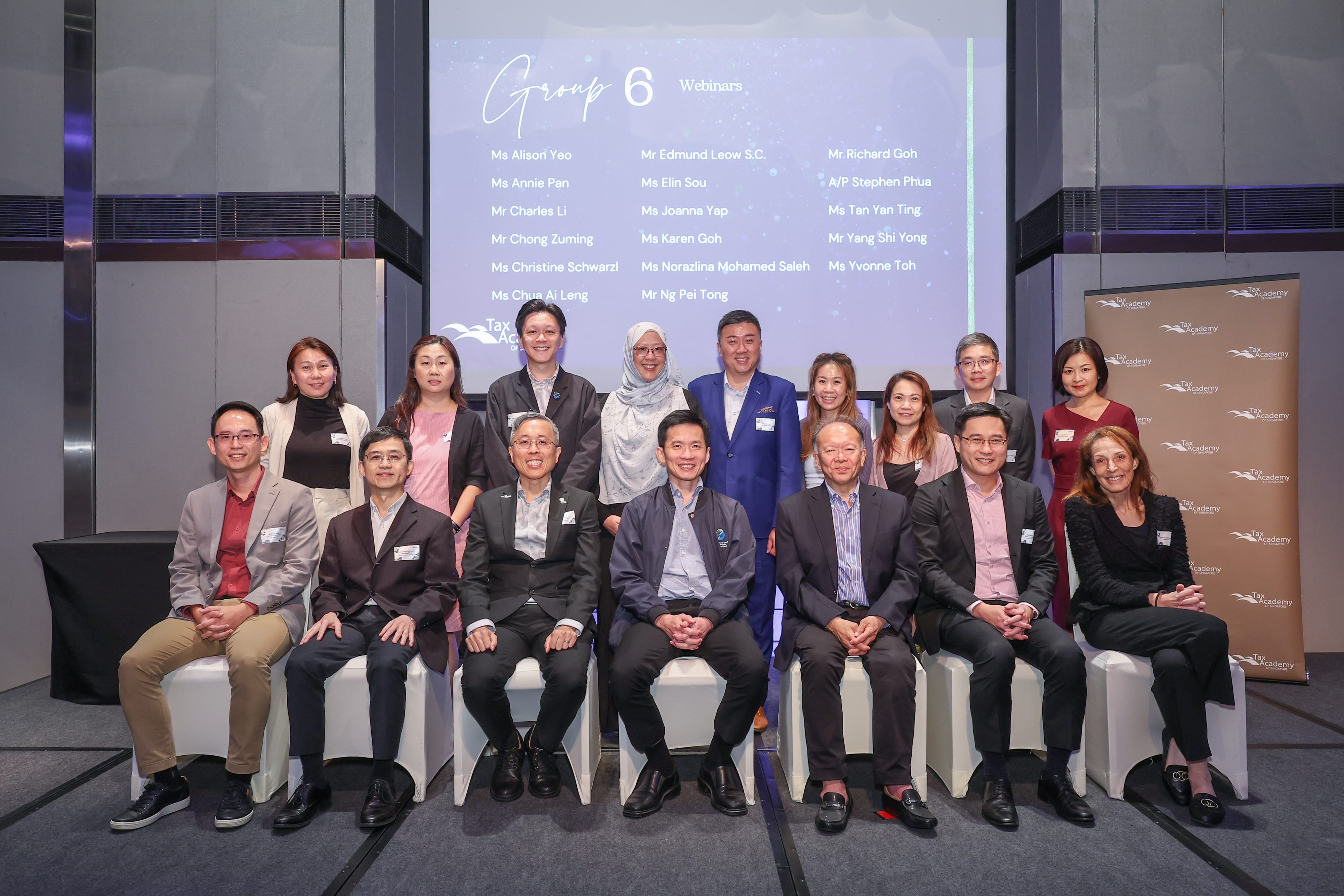 Group of about 15 professionals posing for a photo in front of a screen displaying "Group 6 Webinars" at a Tax Academy event.