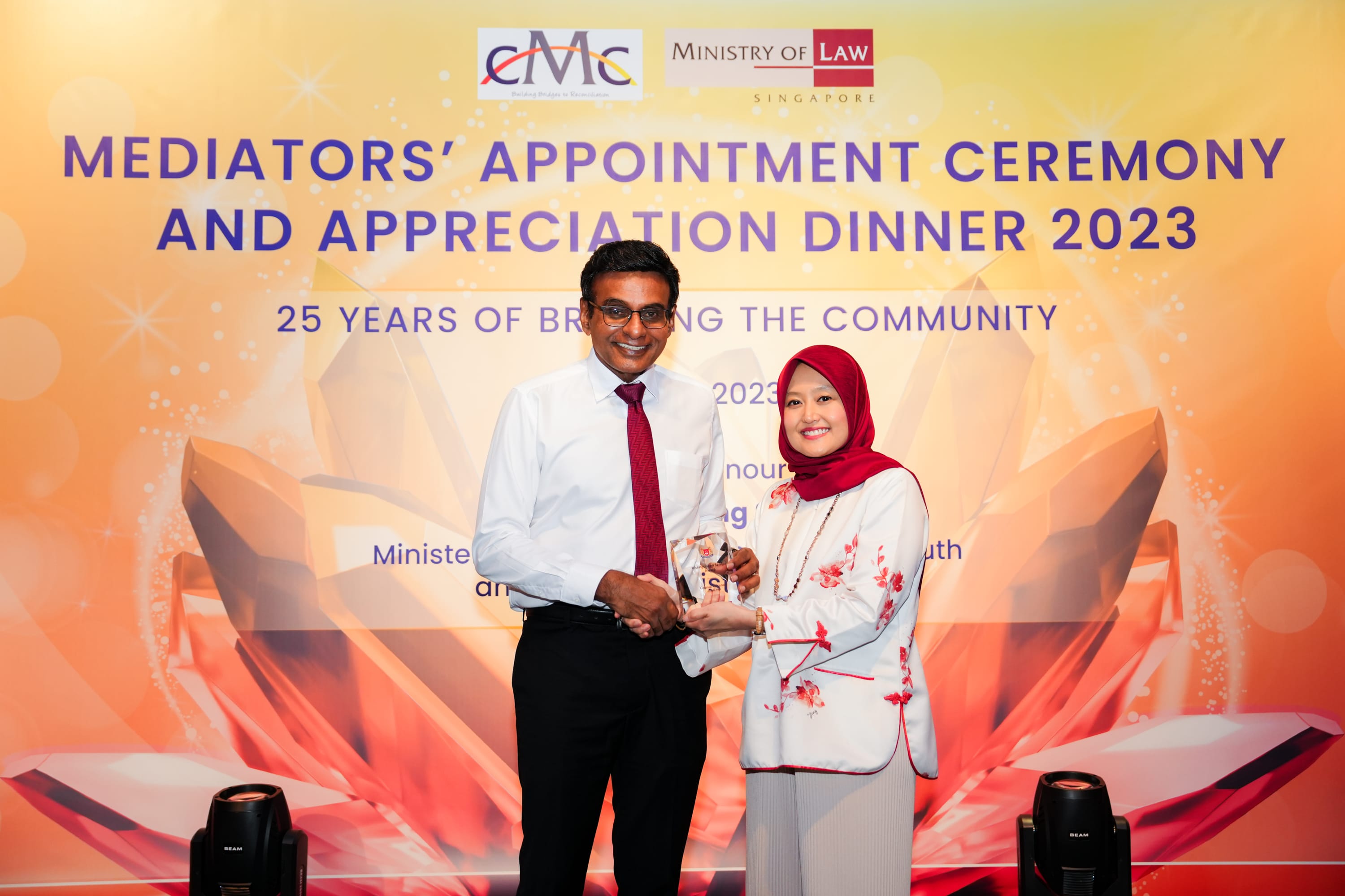 Two people shake hands and hold a trophy at the Mediators' Appointment Ceremony and Appreciation Dinner 2023.