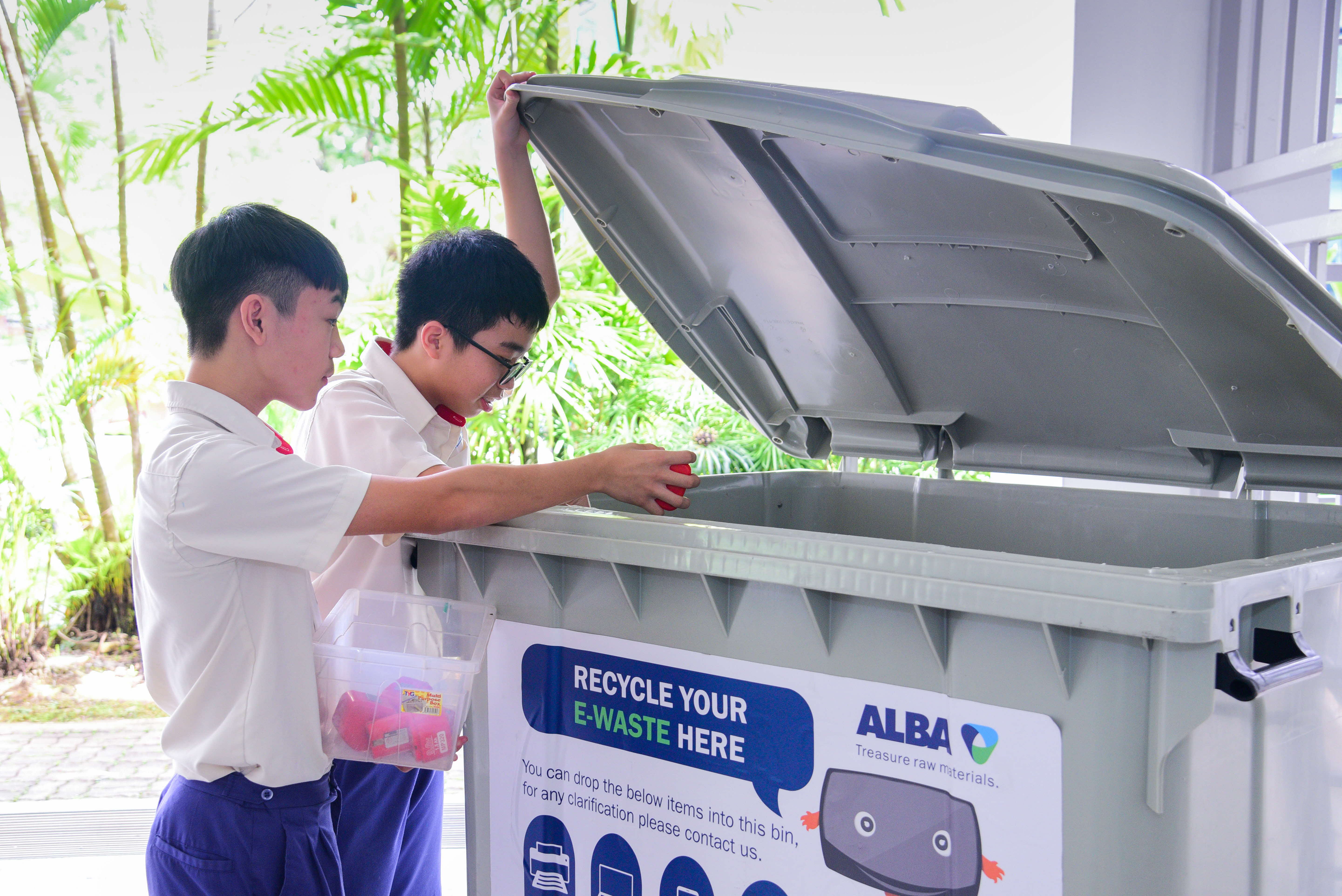 two boys placing e-waste into a recycling bin