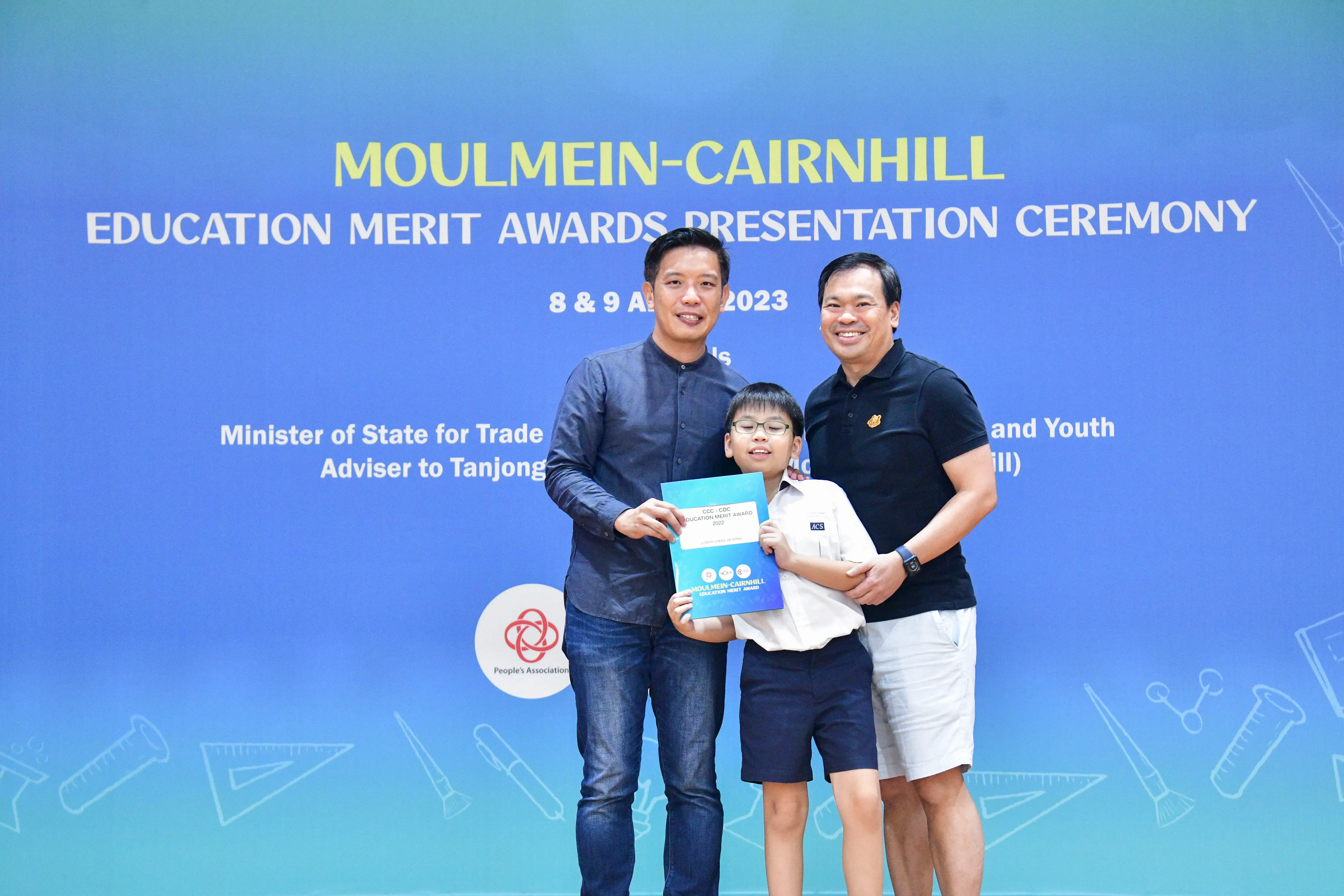 Two men and a boy holding a certificate pose at the Moulmein-Cairnhill Education Merit Awards Ceremony 2023.