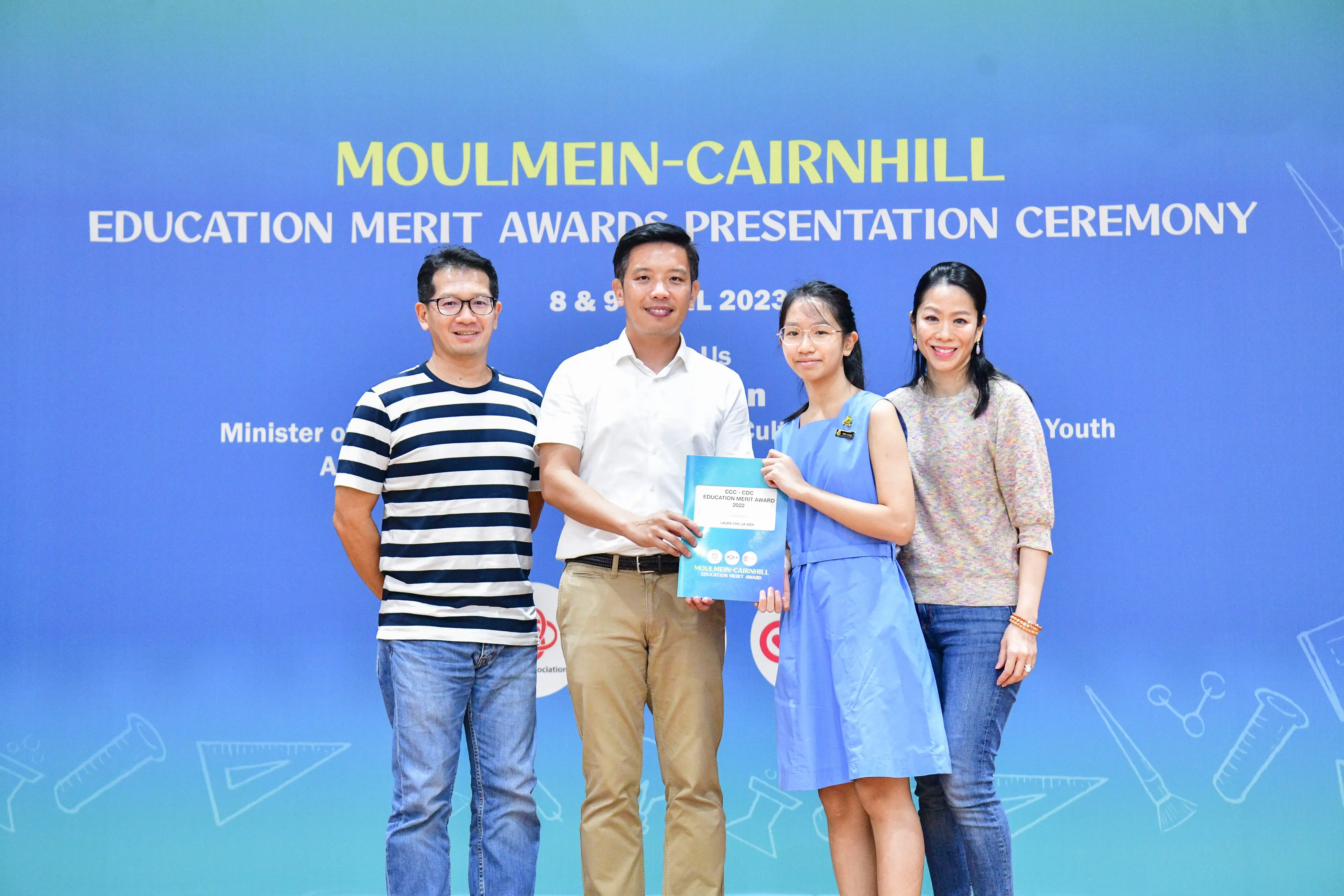 Four people pose together at the Moulmein-Cairnhill Education Merit Awards Presentation Ceremony, one holding a certificate.