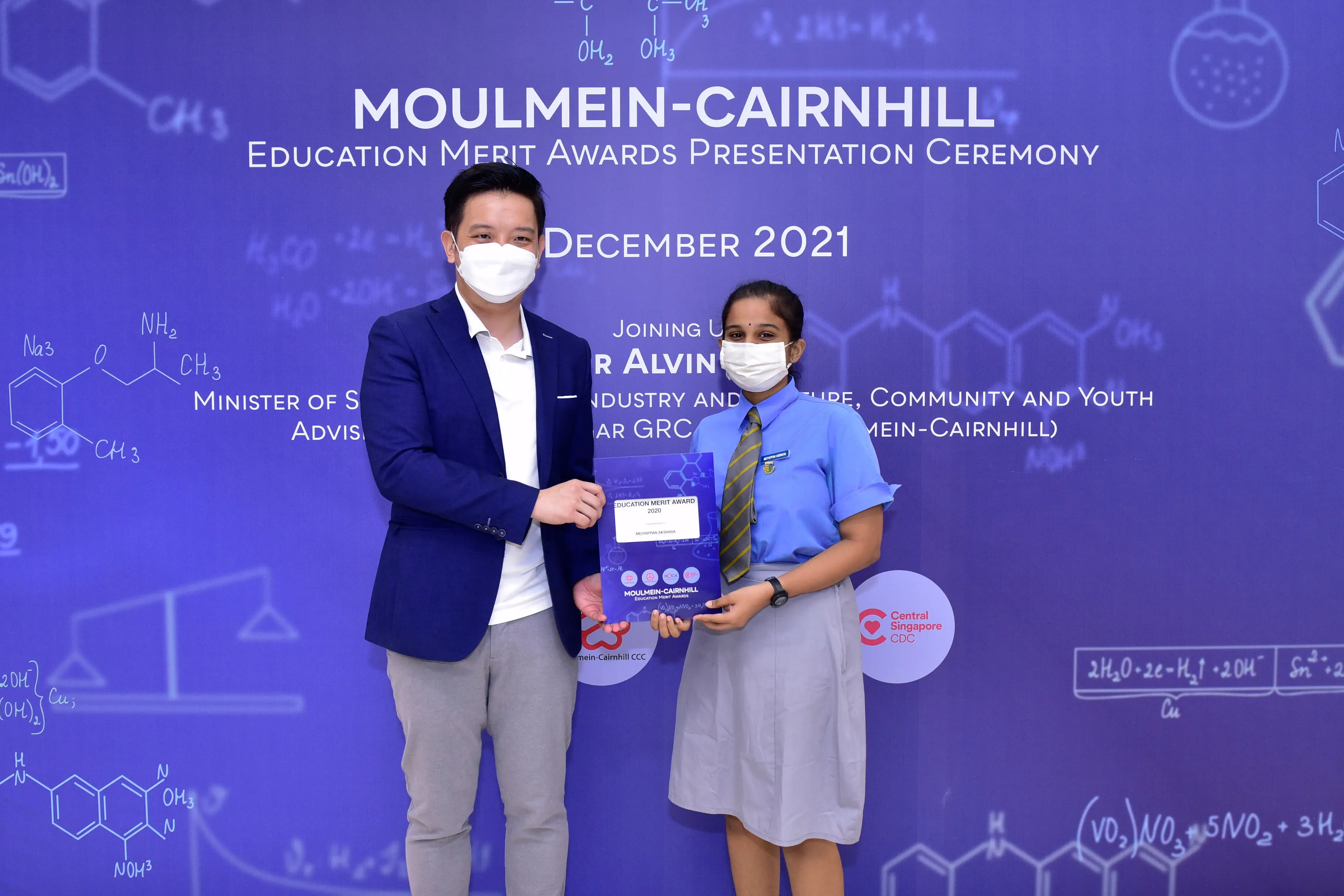 Two masked people hold an award certificate at the Moulmein-Cairnhill Education Merit Awards Ceremony, December 2021.