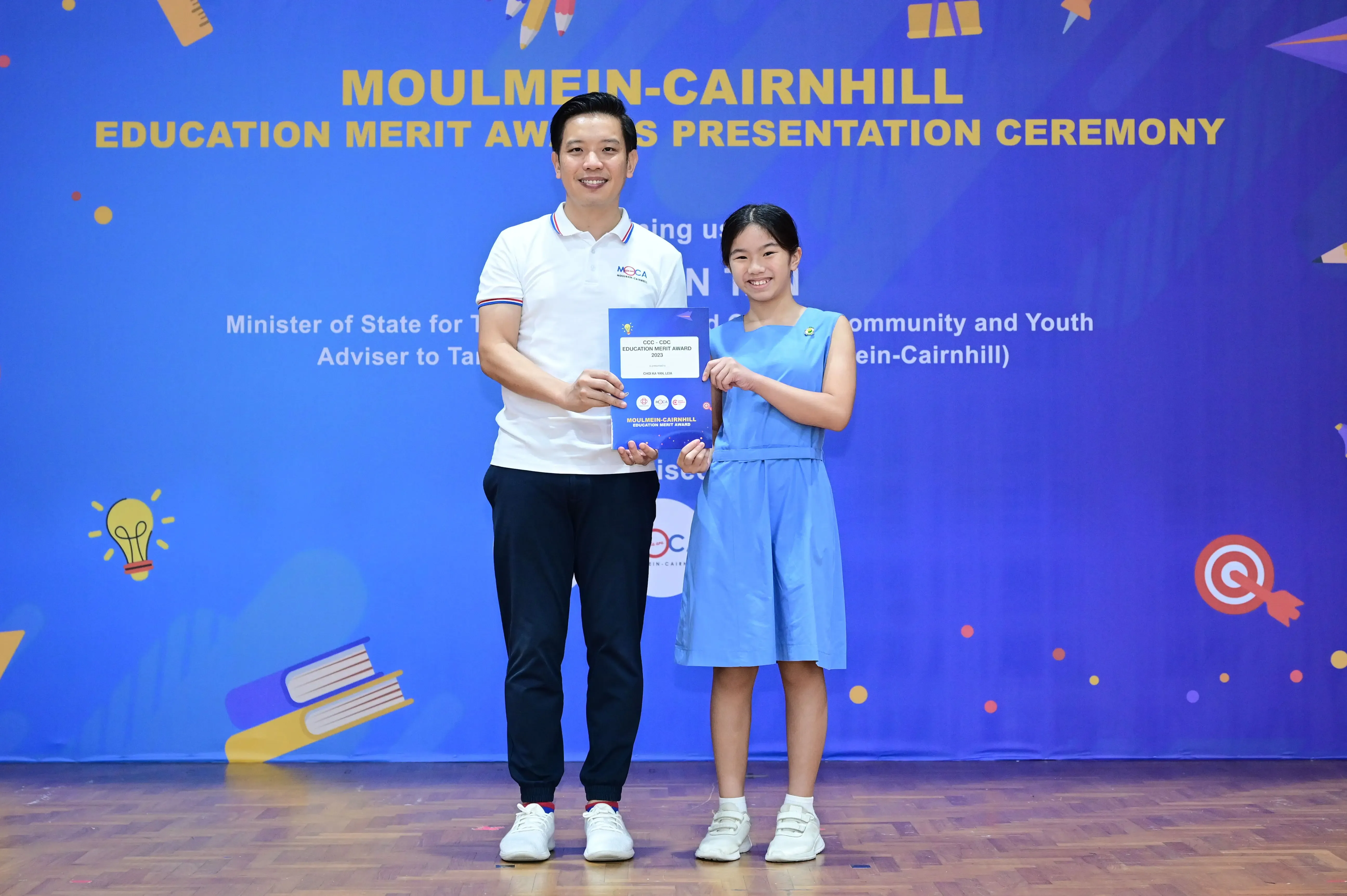A man and a young girl hold an award certificate at the Moulmein-Cairnhill Education Merit Award Presentation Ceremony.