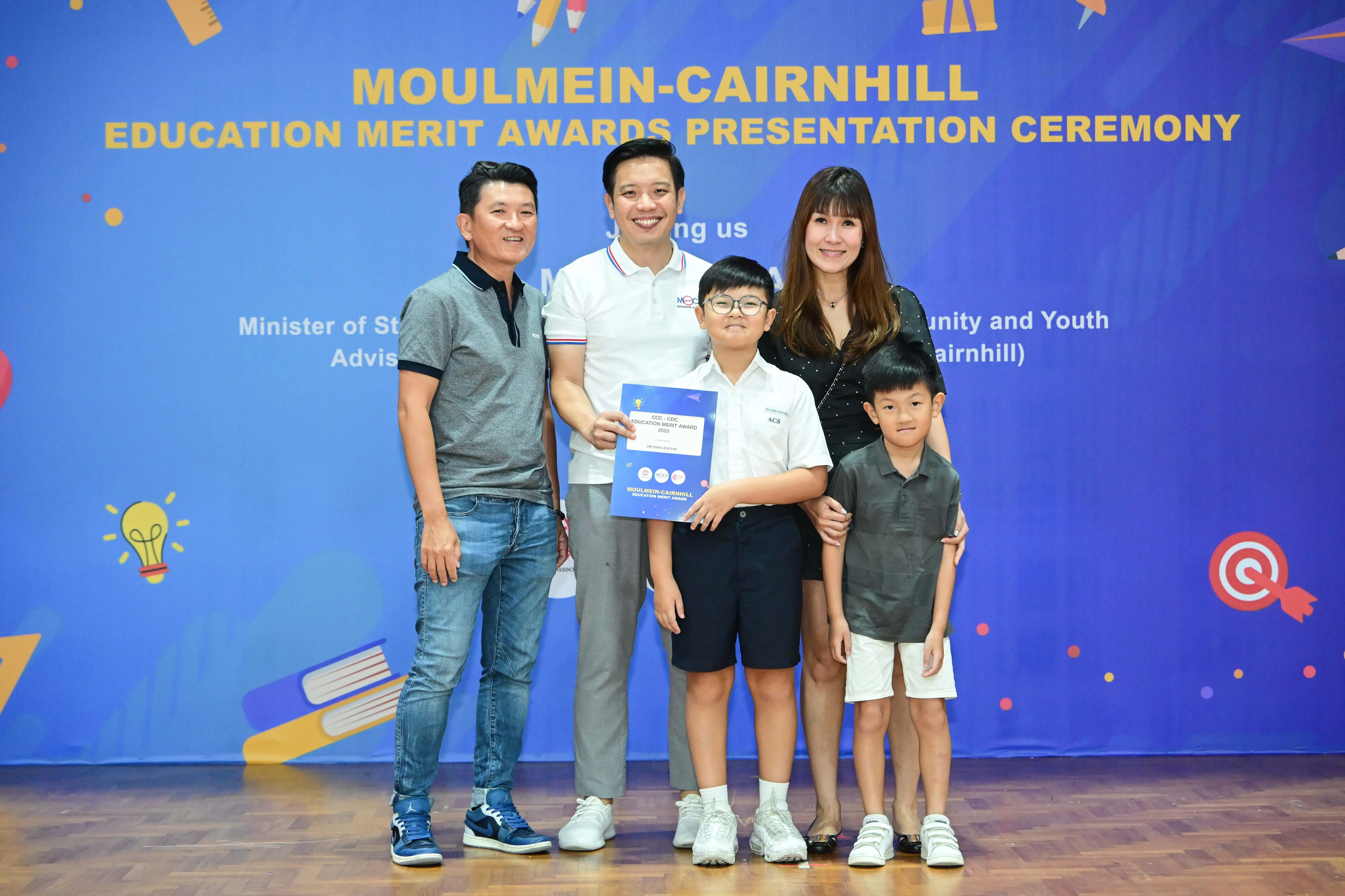 Five people pose at the Moulmein-Cairnhill Education Merit Awards Presentation Ceremony, with a boy holding a certificate.