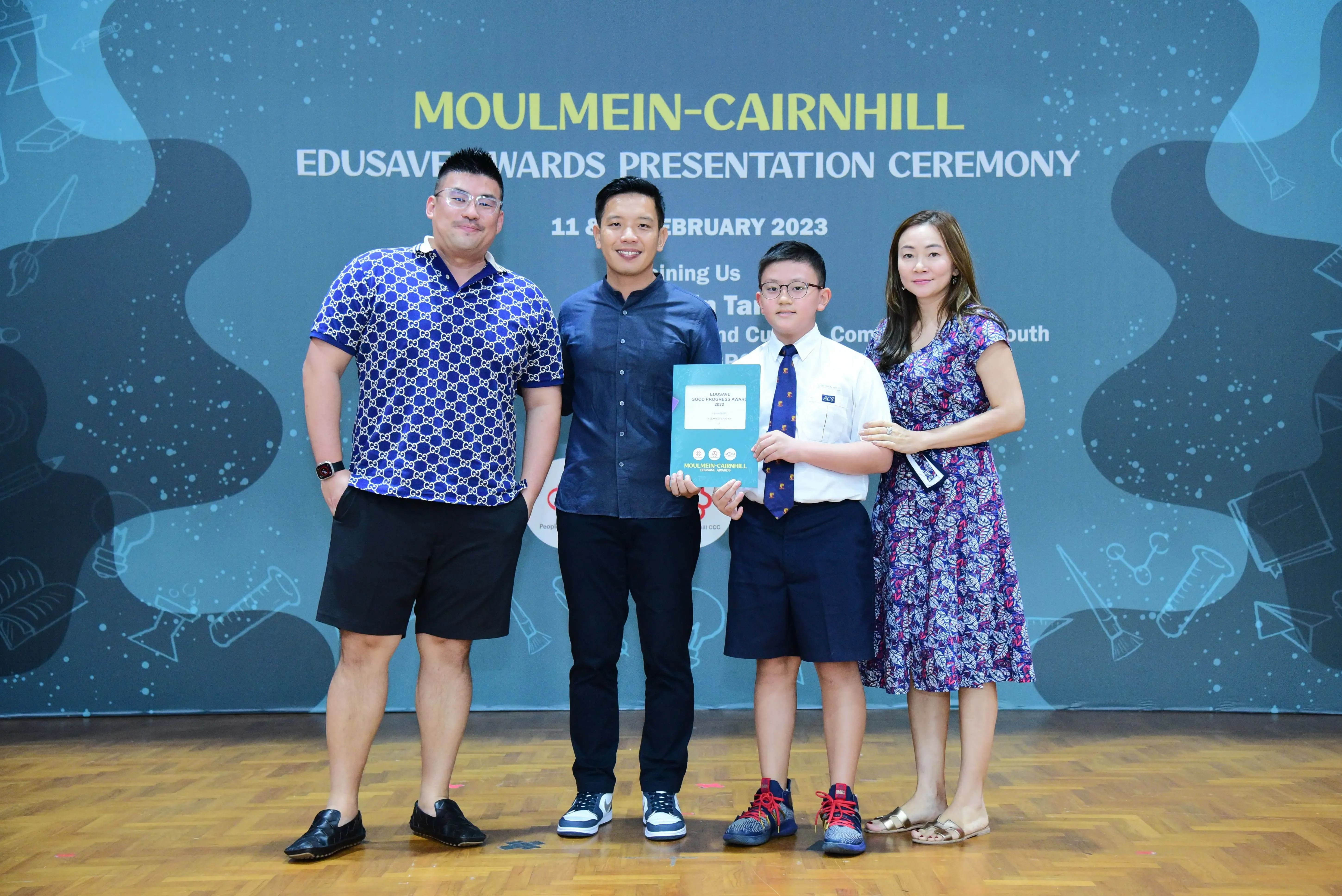 Four people pose at the Moulmein-Cairnhill Edusave Awards Presentation Ceremony, with a boy holding a certificate.