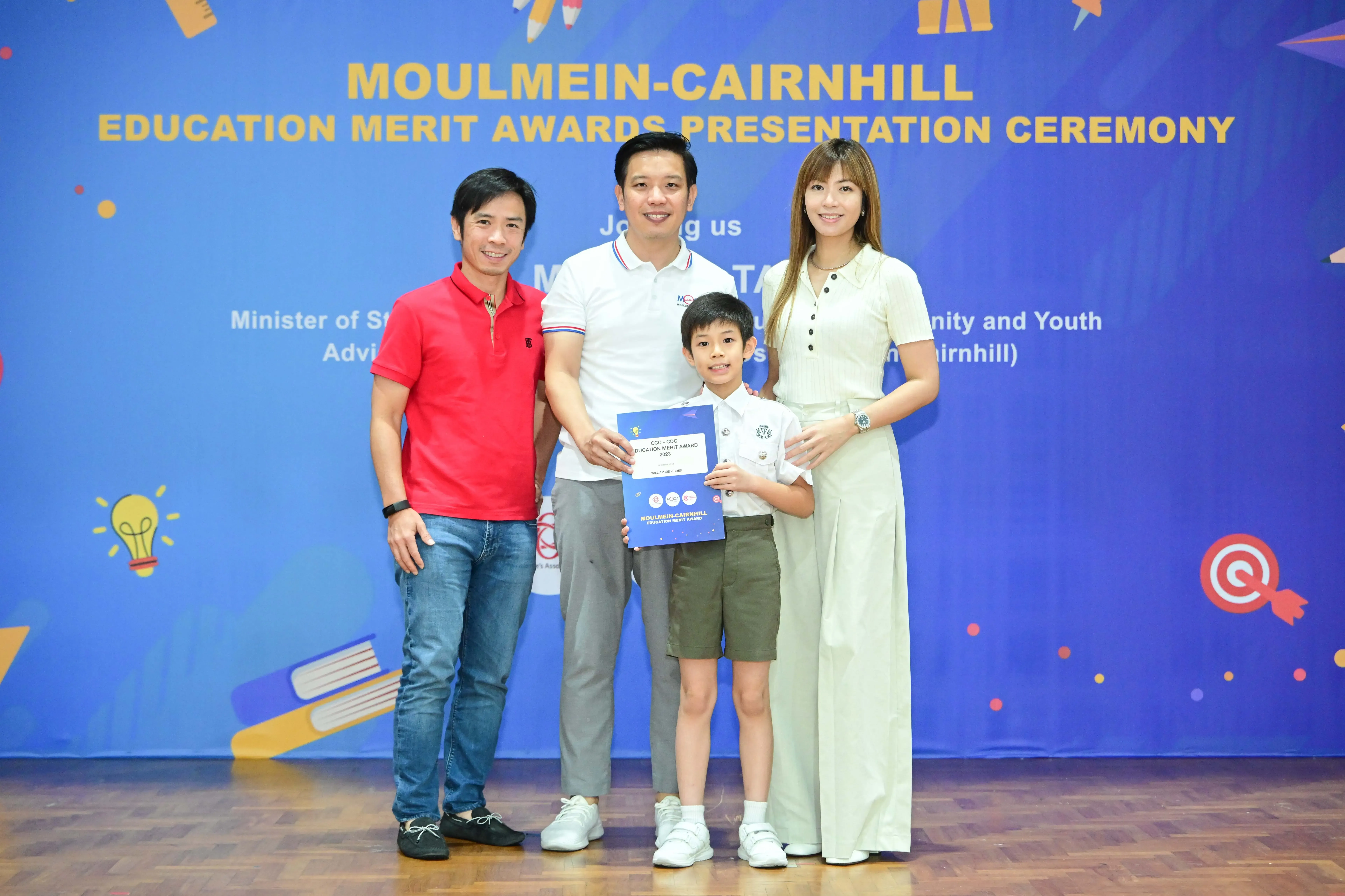 Three adults and a young boy pose with an award certificate at the Moulmein-Cairnhill Education Merit Awards ceremony.
