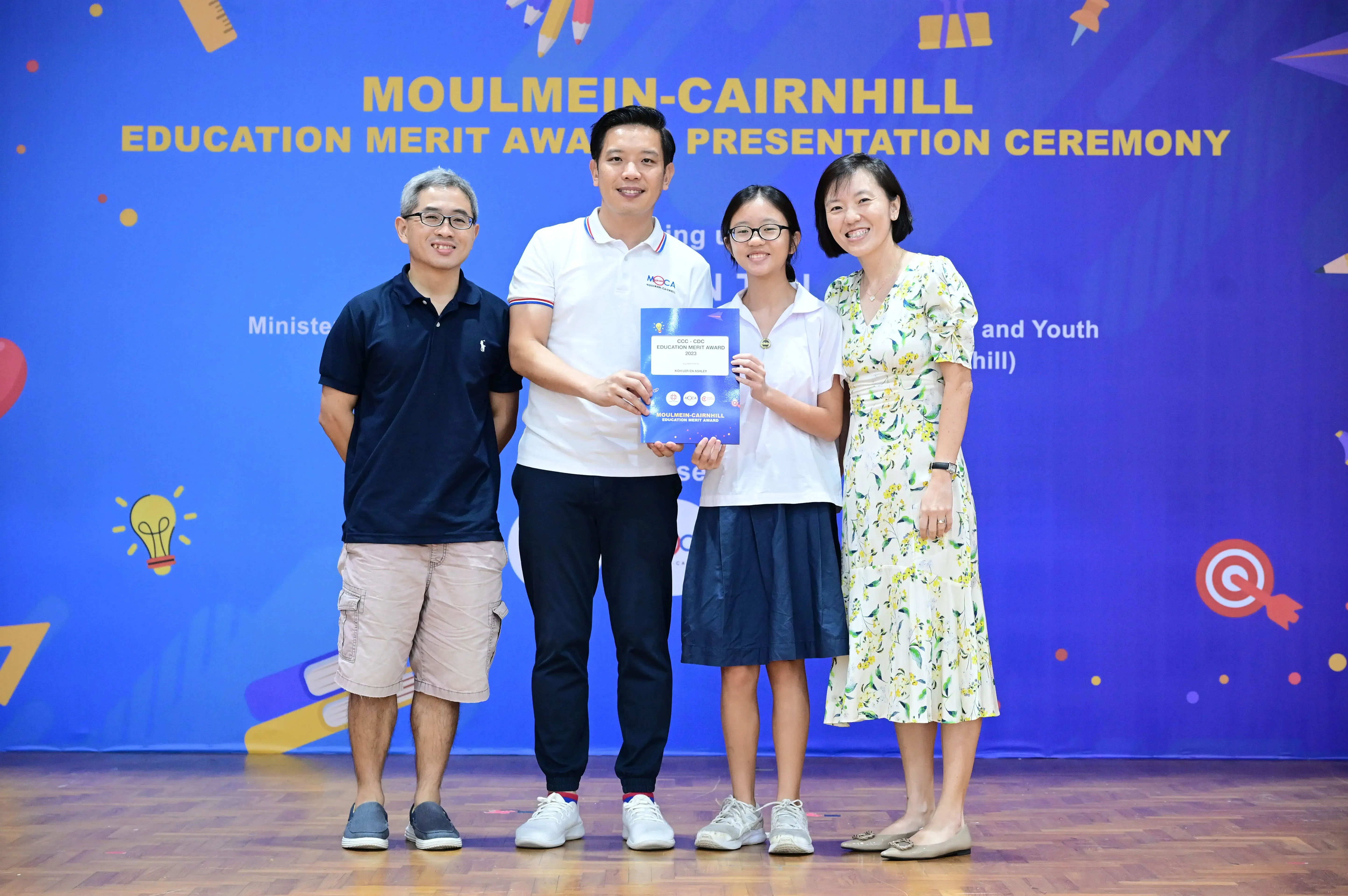 Four people pose at the Moulmein-Cairnhill Education Merit Award Presentation Ceremony, holding an award certificate.