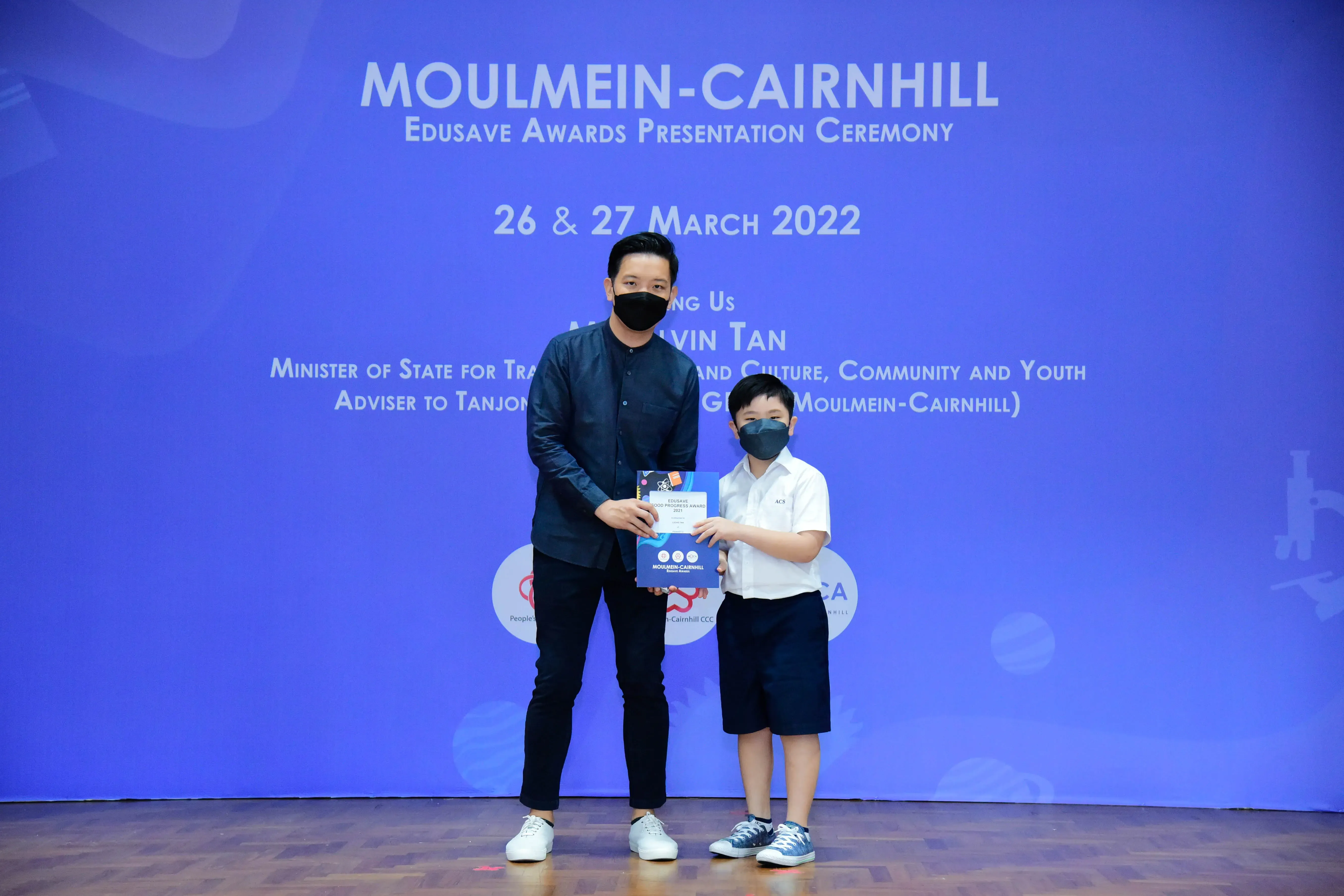An adult and a young boy in masks hold an award at the Moulmein-Cairnhill Edusave Awards Ceremony, March 2022.