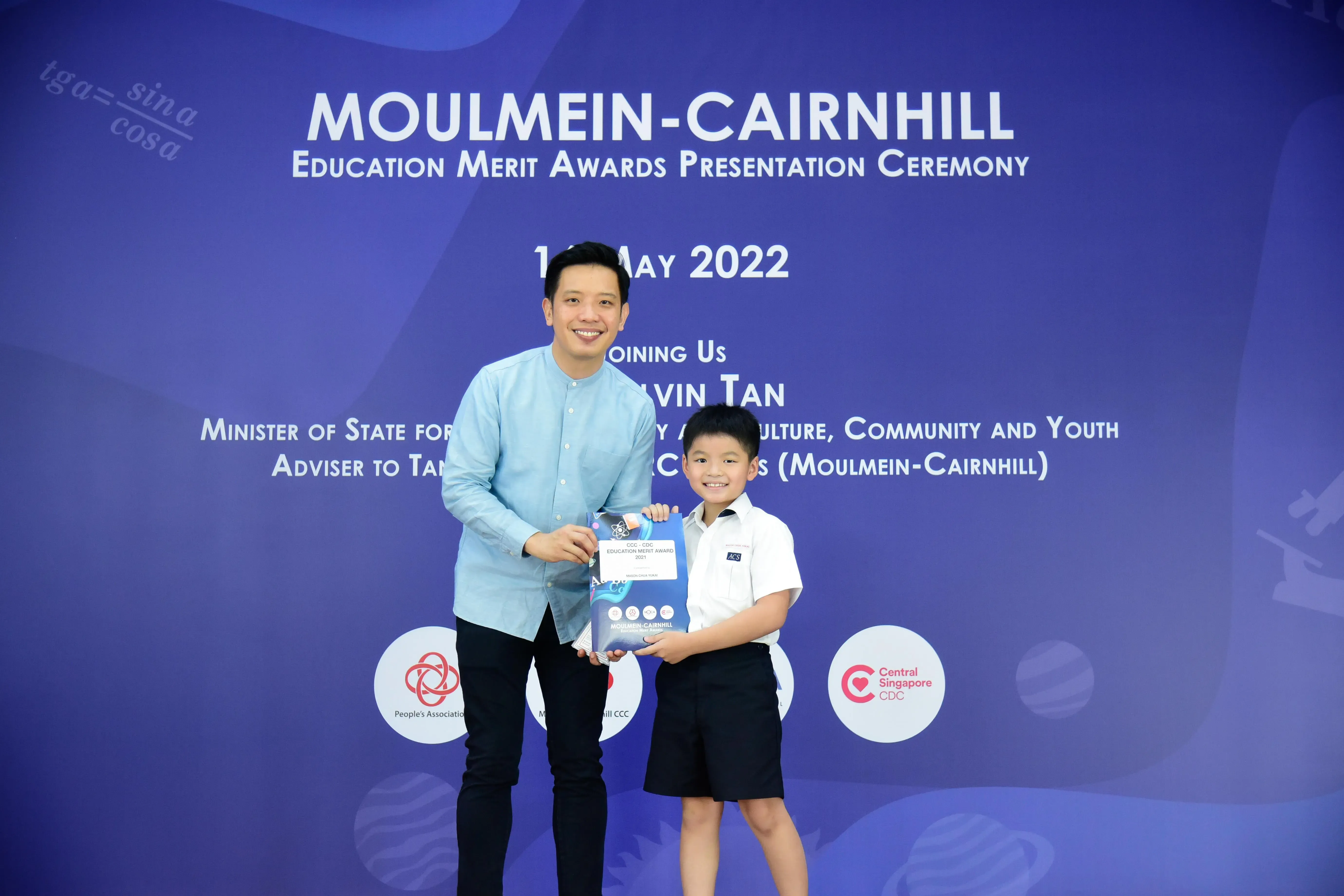 A man and a young boy hold an award together at the Moulmein-Cairnhill Education Merit Awards Ceremony, May 2022.