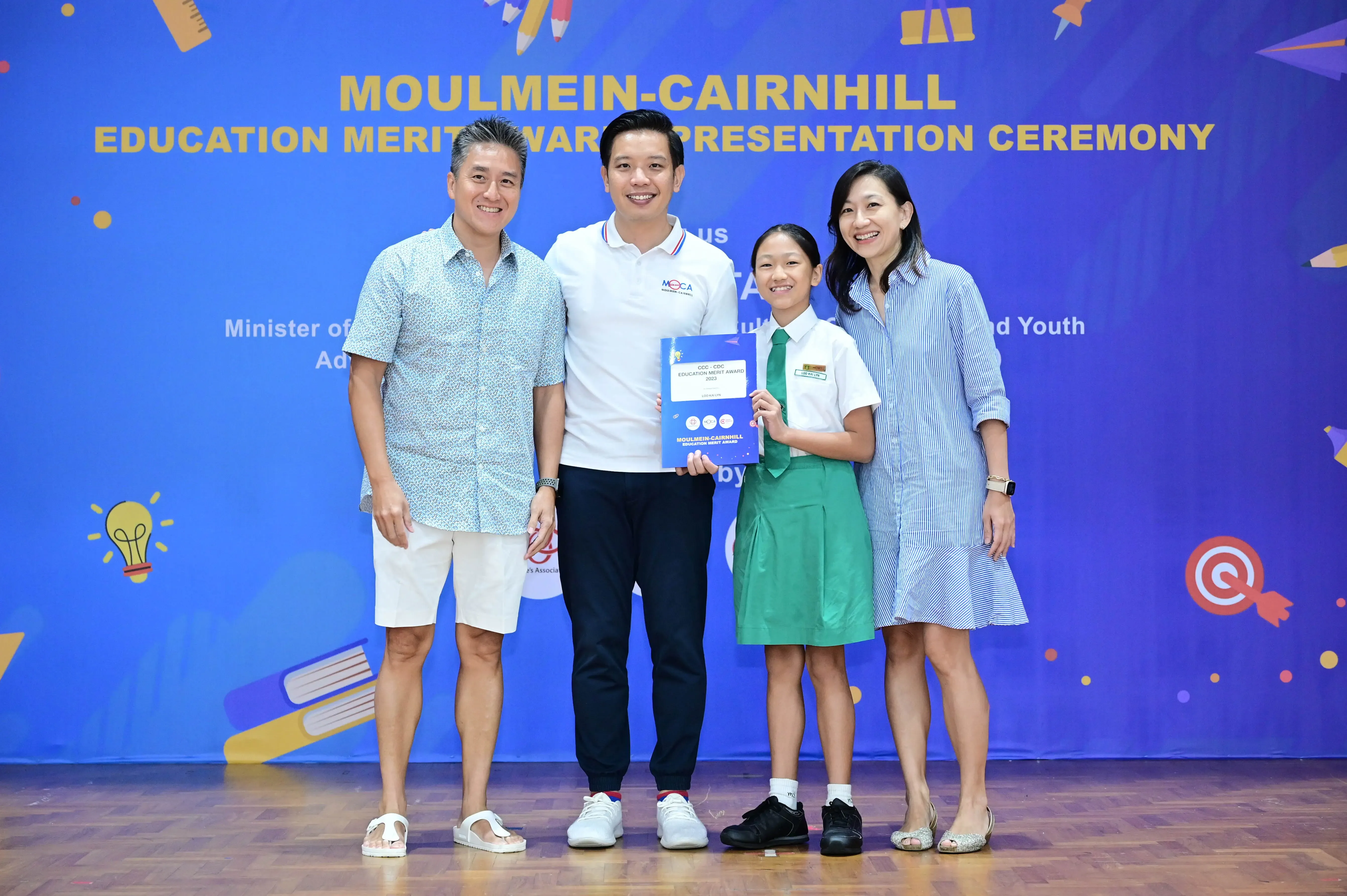 Four people pose at the Moulmein-Cairnhill Education Merit Award Presentation Ceremony, with a student holding a certificate.