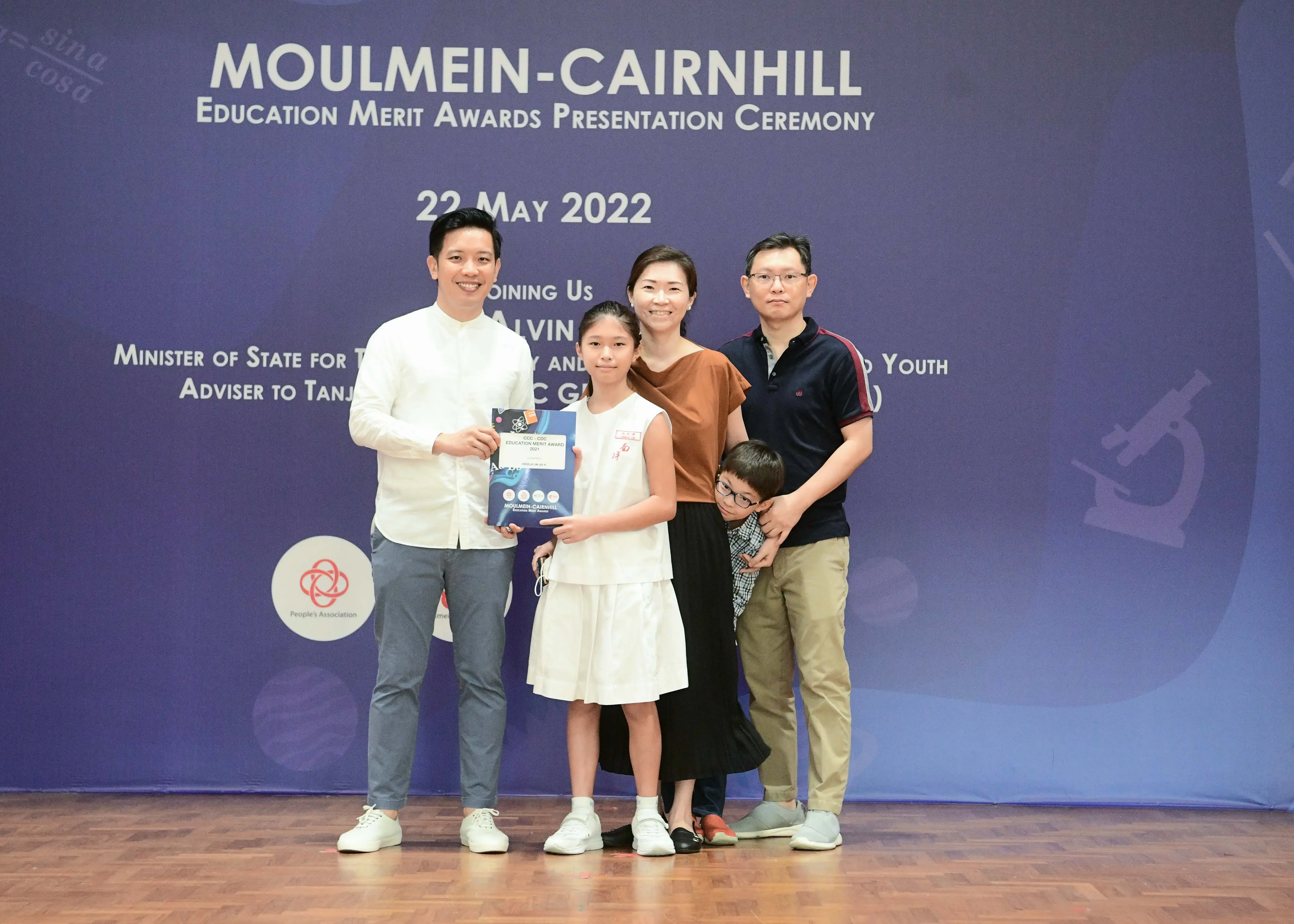 Five people pose in front of a Moulmein-Cairnhill Education Merit Awards banner dated 22 May 2022.