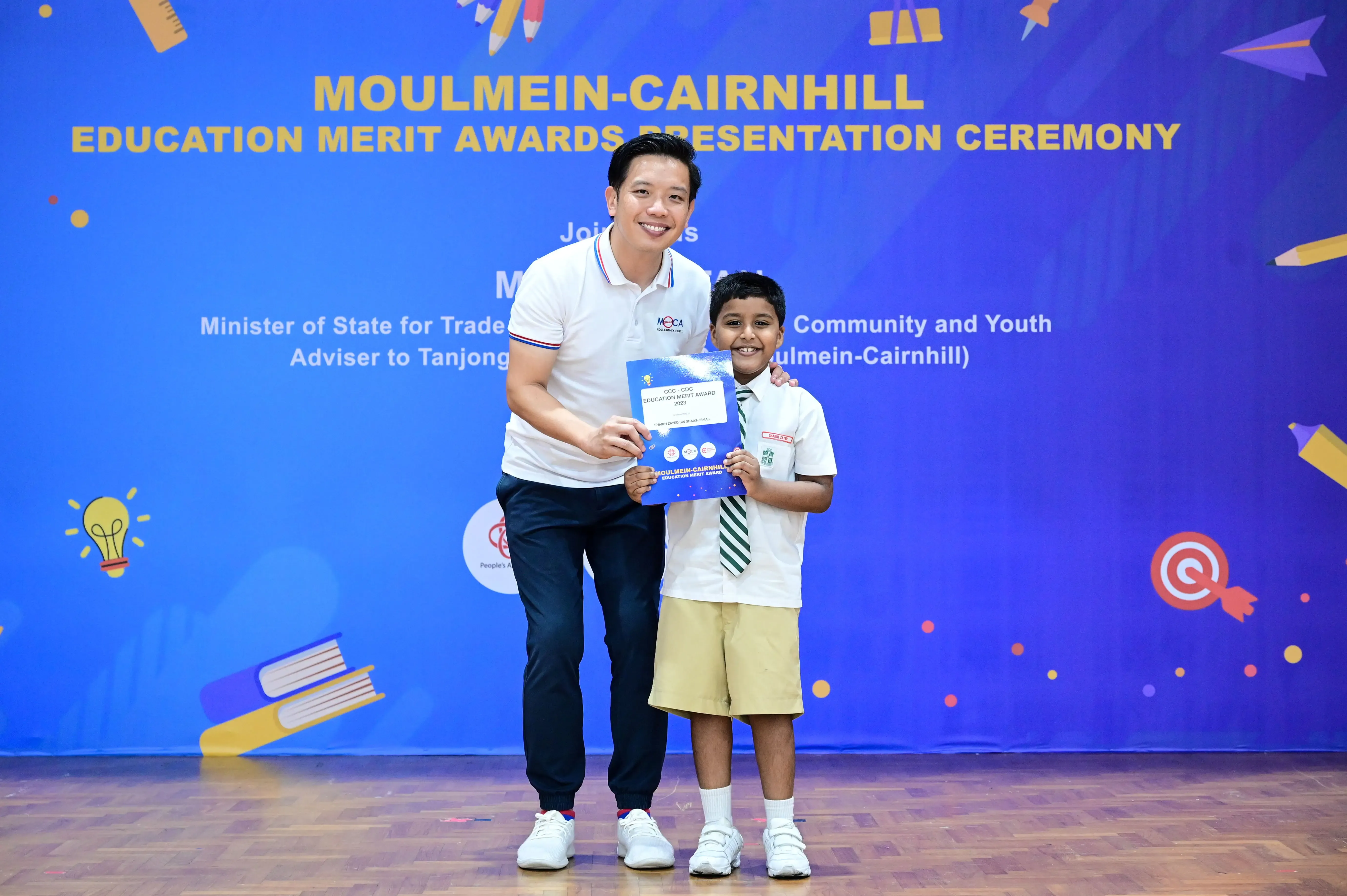 A man and a young boy hold an award certificate at the Moulmein-Cairnhill Education Merit Awards Presentation Ceremony.