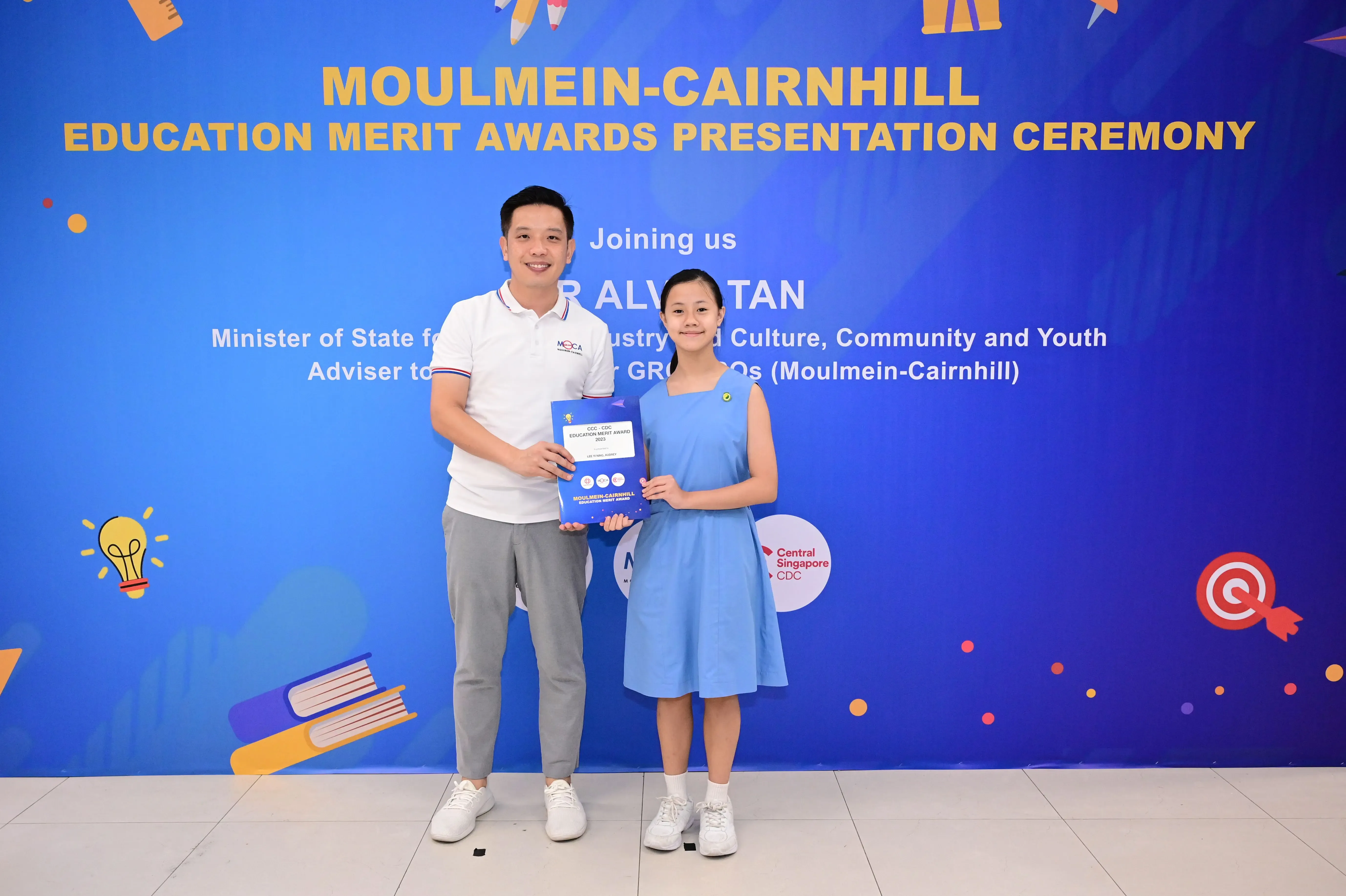 A man and a young girl hold an award certificate at the Moulmein-Cairnhill Education Merit Awards Presentation Ceremony.