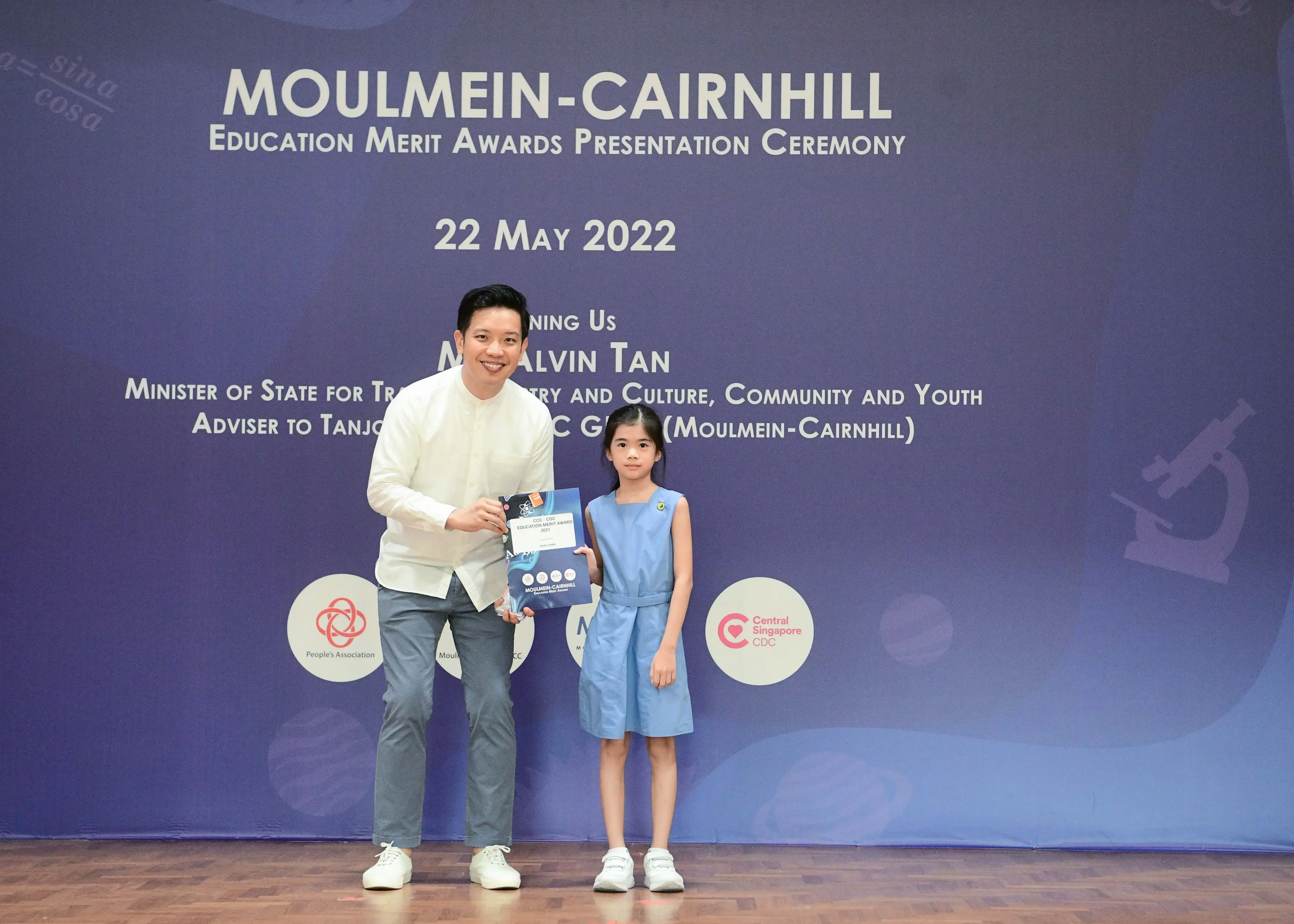 A man and a young girl pose together holding an award at the Moulmein-Cairnhill Education Merit Awards ceremony on 22 May 2022.