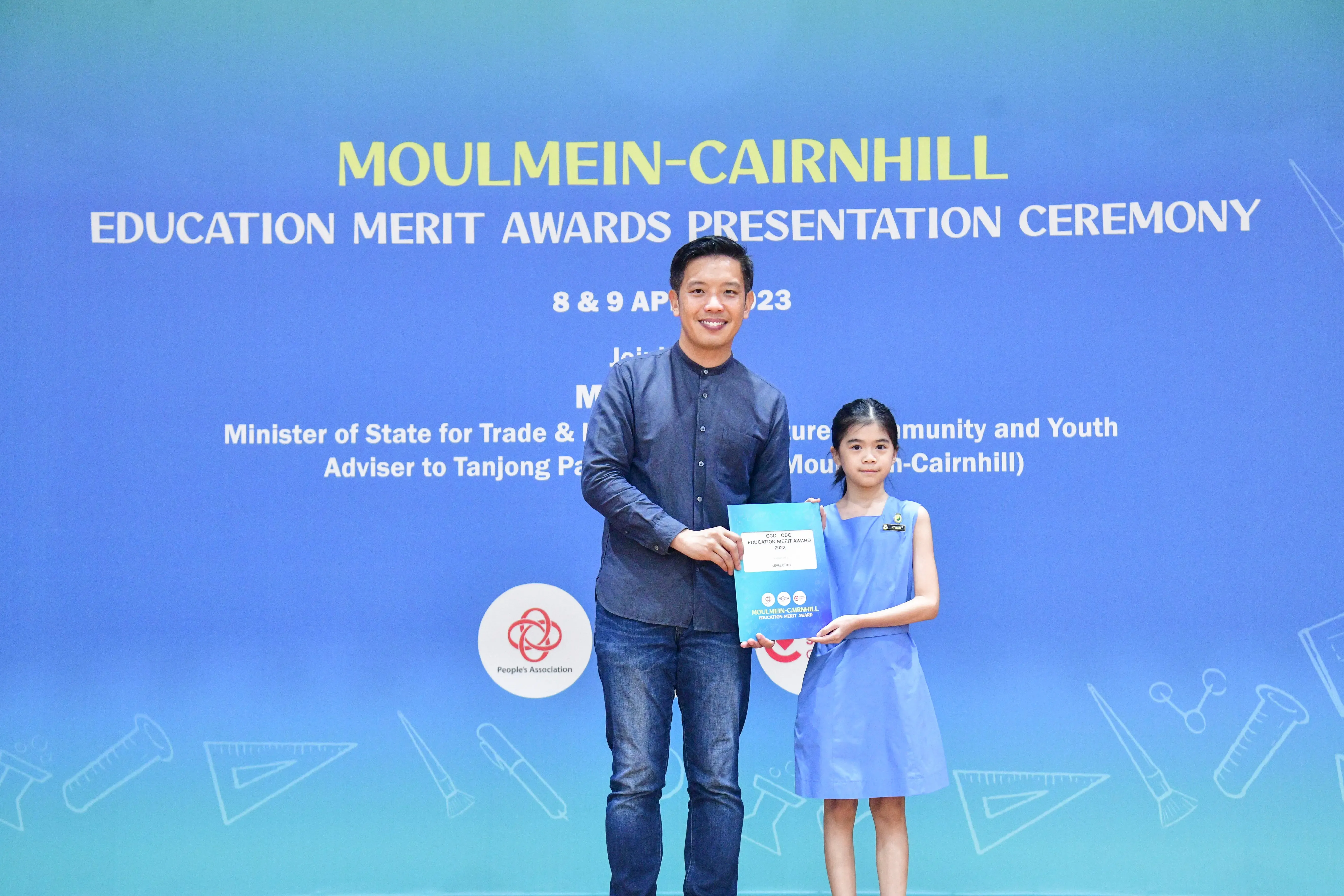 A man and a young girl hold an award certificate at the Moulmein-Cairnhill Education Merit Awards Ceremony 2023.