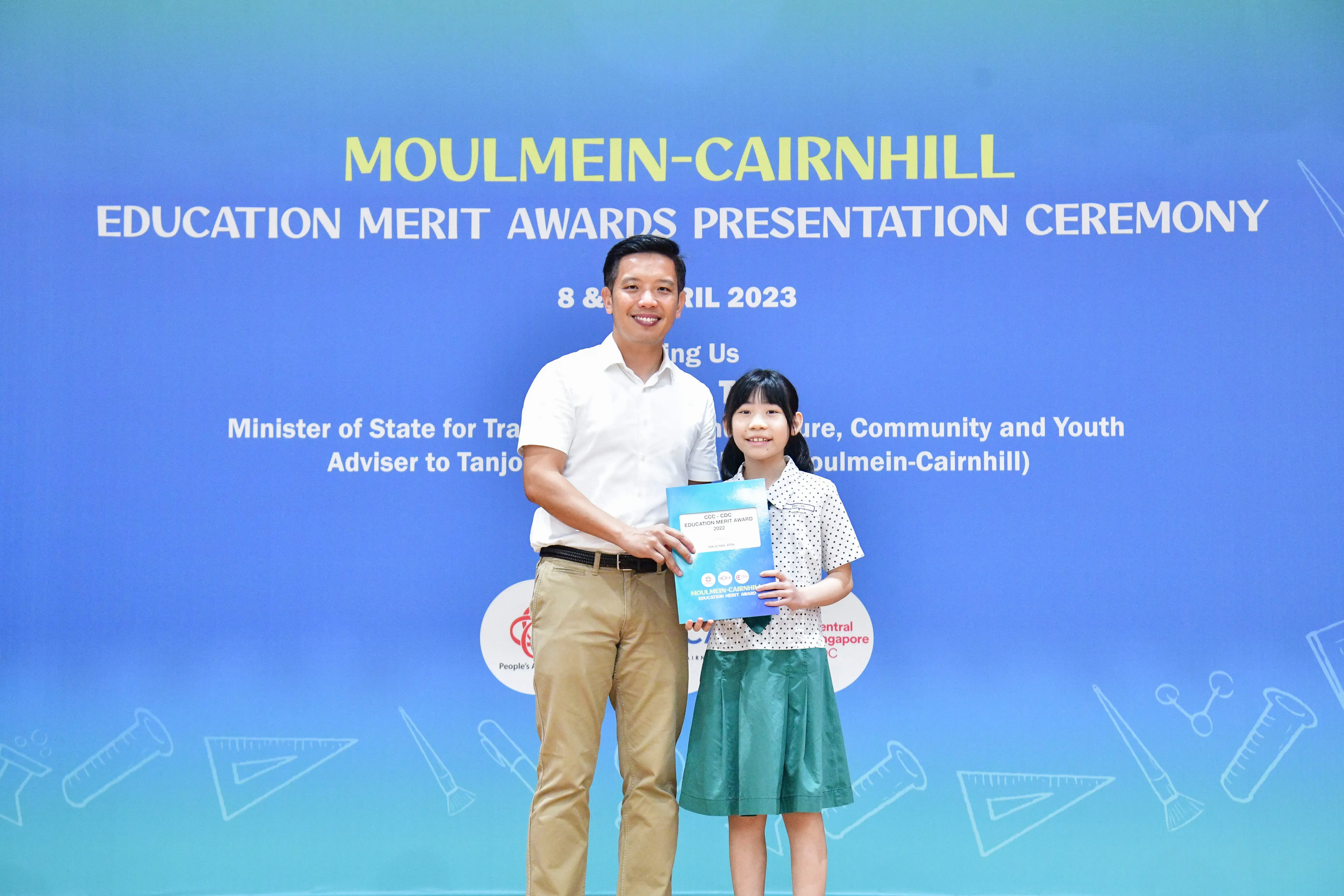 A man and a young girl hold a certificate together at the Moulmein-Cairnhill Education Merit Awards ceremony in April 2023.