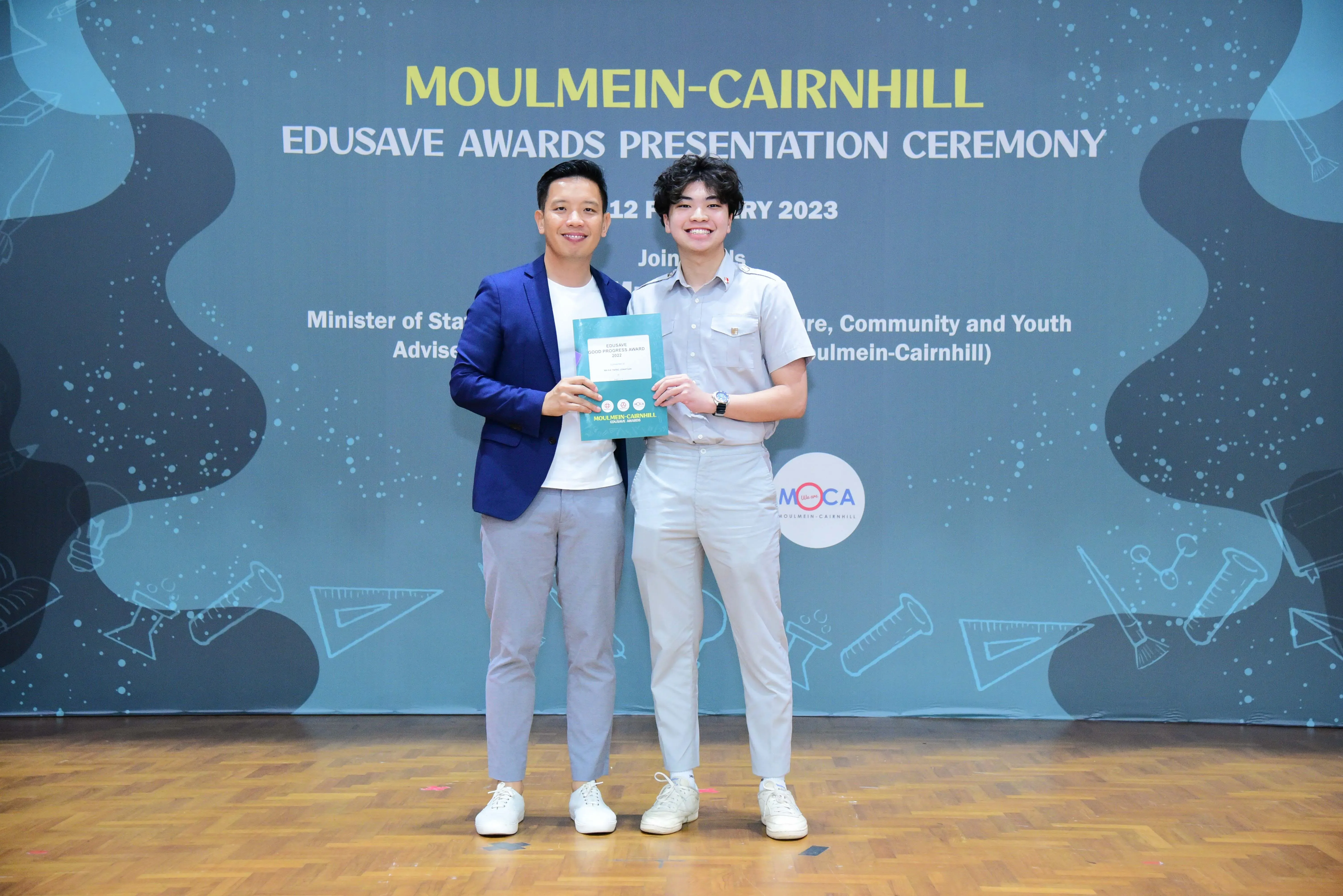 Two men smile and hold a certificate at the Moulmein-Cairnhill Edusave Awards Presentation Ceremony 2023.
