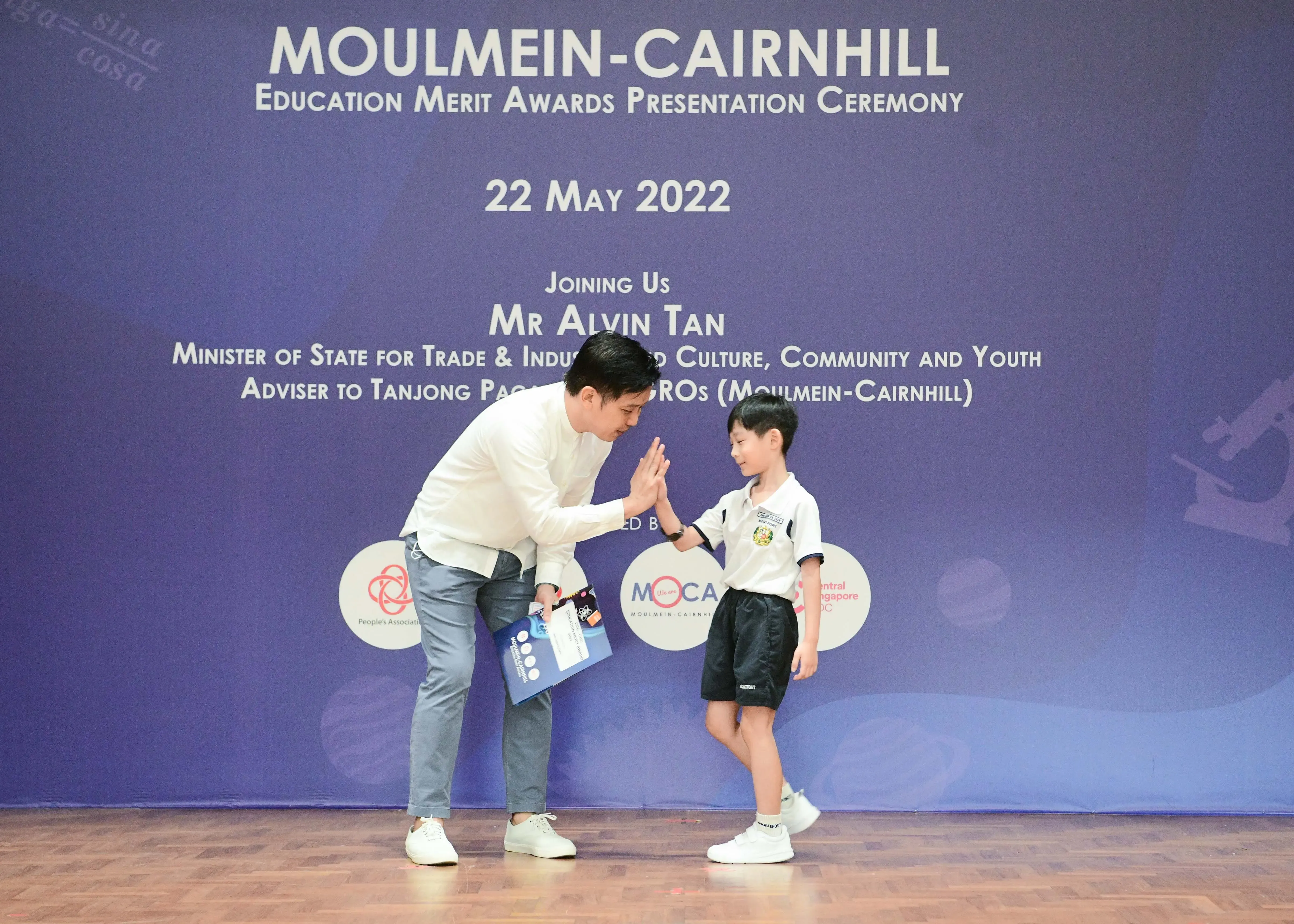 An adult man high-fives a young boy in school uniform at the Moulmein-Cairnhill Education Merit Awards 2022.