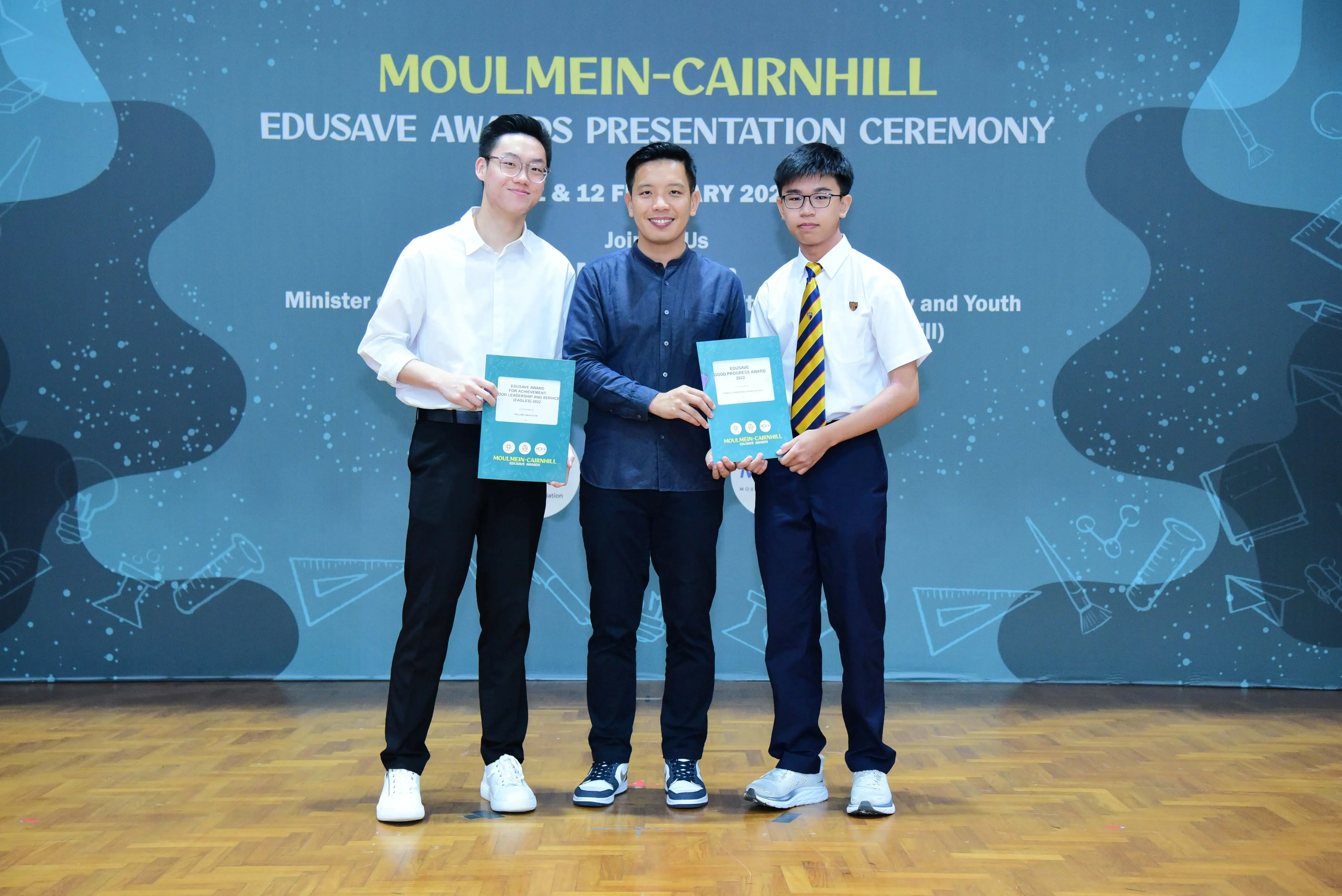 Three people pose holding certificates at the Moulmein-Cairnhill Edusave Awards Presentation Ceremony backdrop.